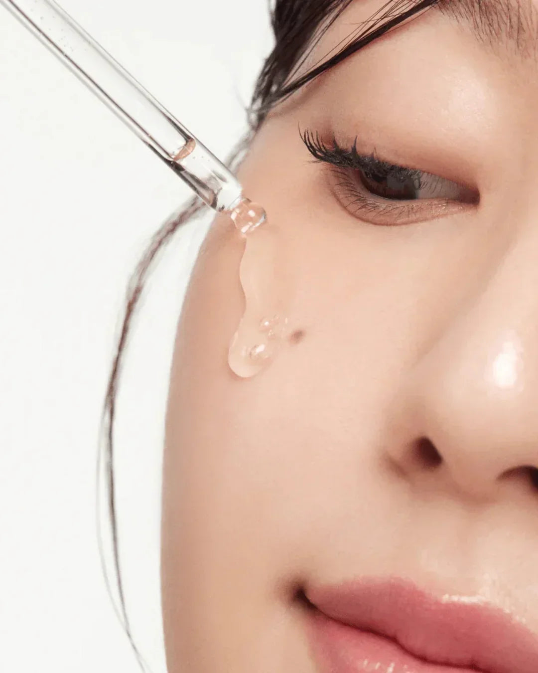 Close-up of woman applying clear serum with dropper on smooth skin near eye
