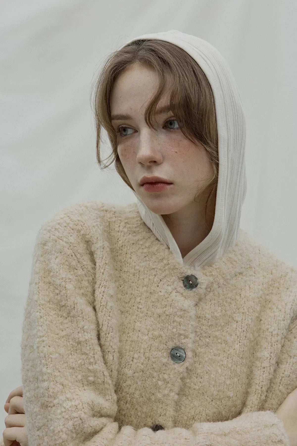 Close-up of woman wearing beige grandmother cardigan and white hooded top against plain background