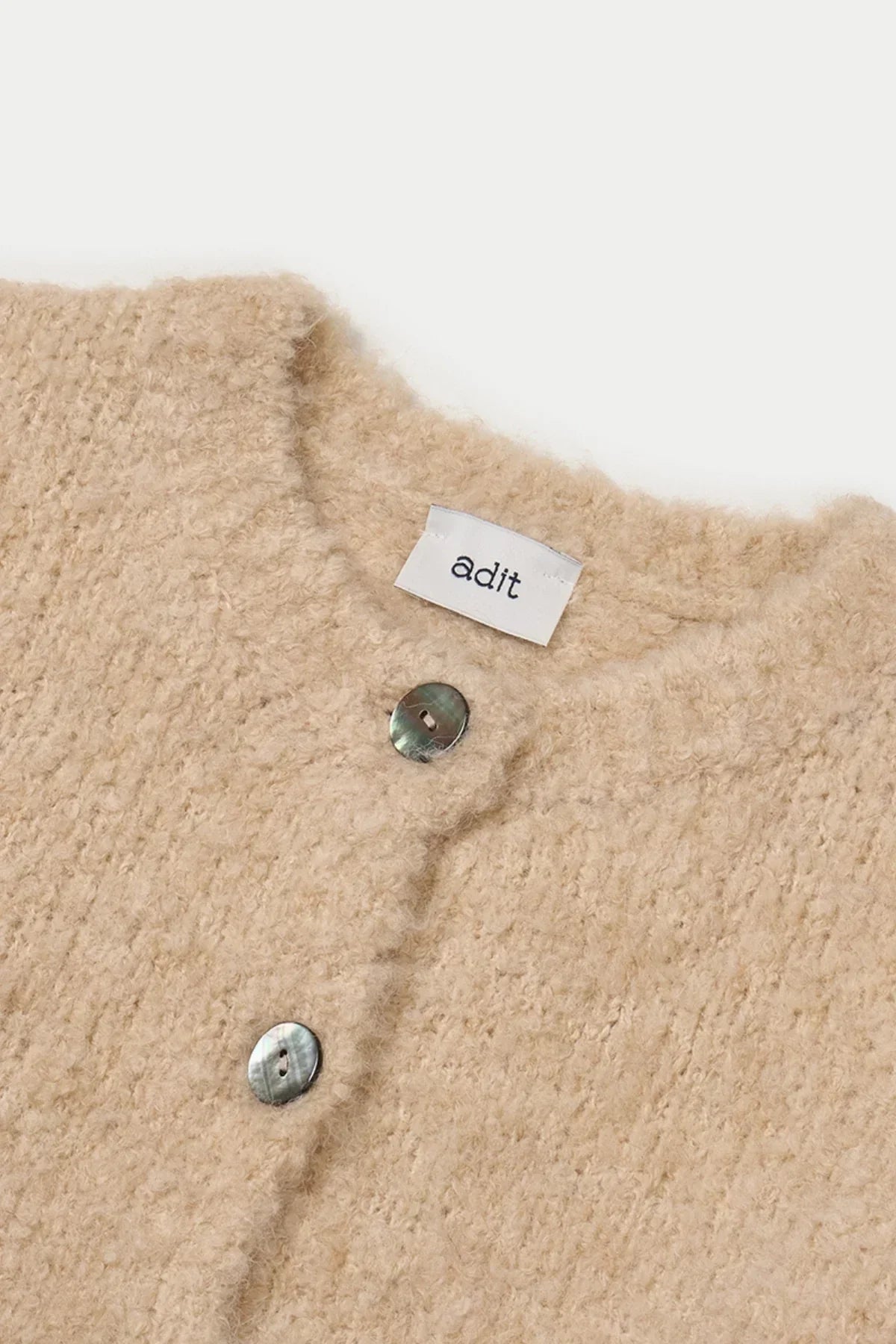 Close-up of beige textured grandma cardigan with iridescent buttons and adit label