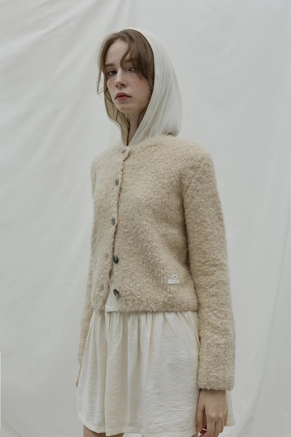 Young woman wearing beige textured grandma cardigan over white hoodie dress in studio
