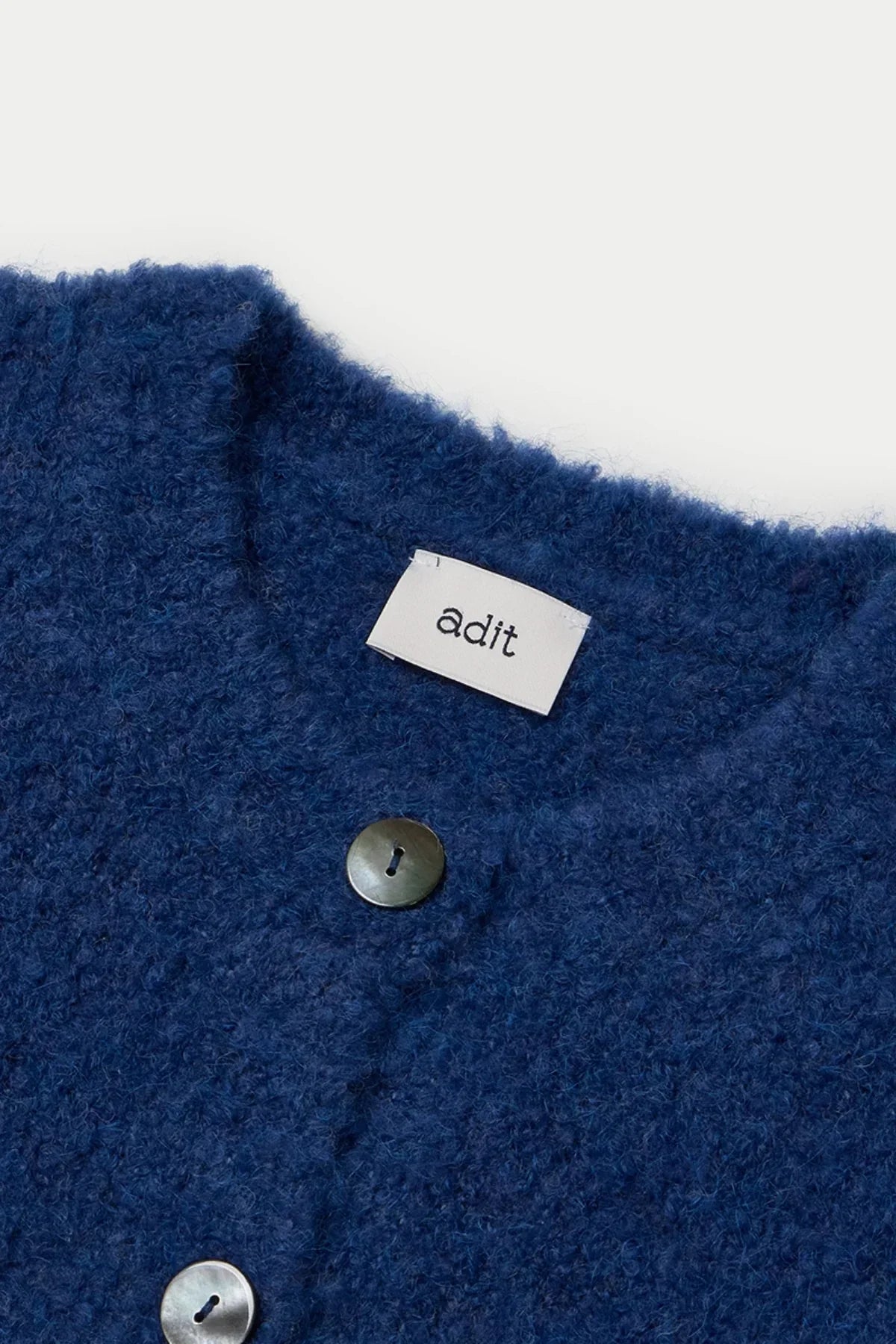 Close-up of a dark blue fuzzy grandma cardigan with mother-of-pearl buttons and an adit label