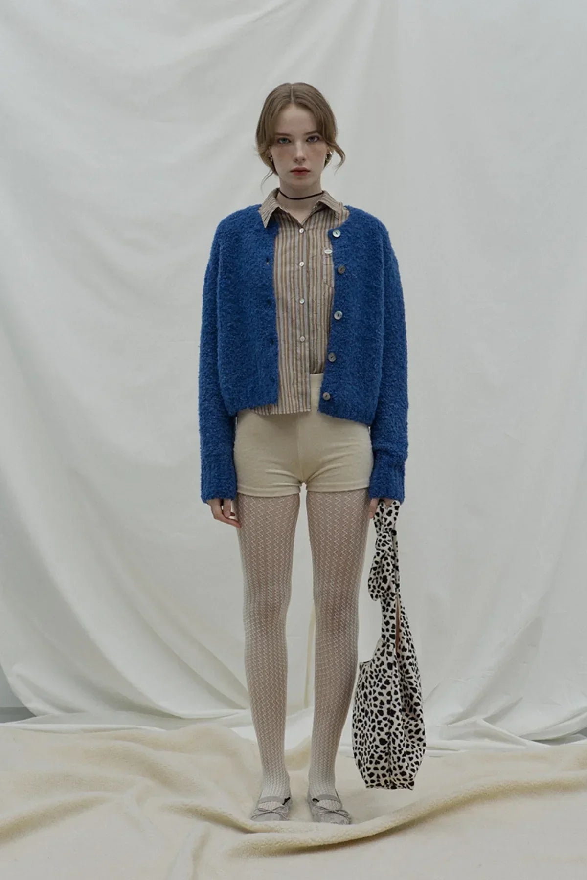 Woman wearing a dark blue fuzzy cardigan over striped shirt with cream shorts and patterned tights