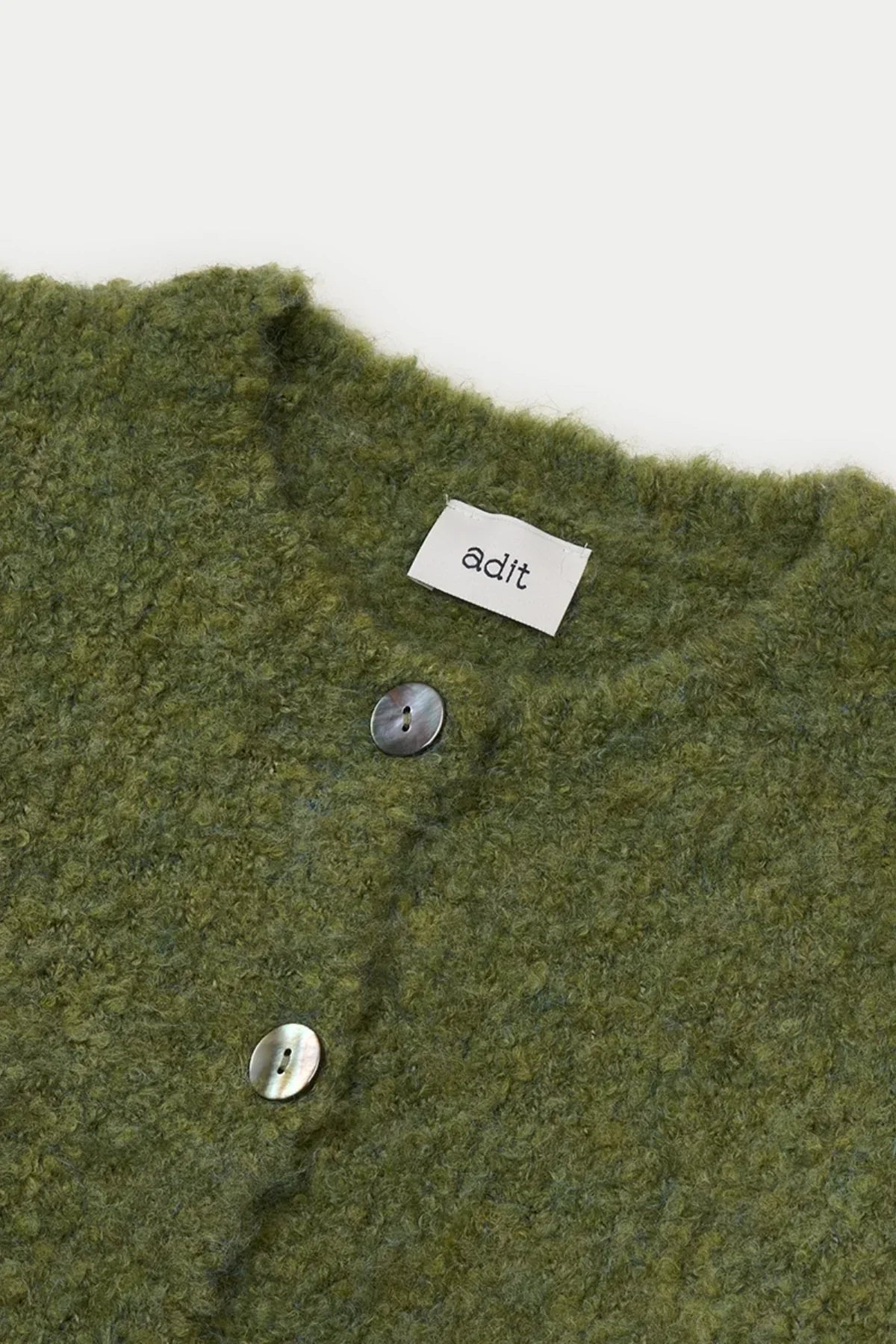 Close-up of green textured grandma cardigan with mother-of-pearl buttons and adit label