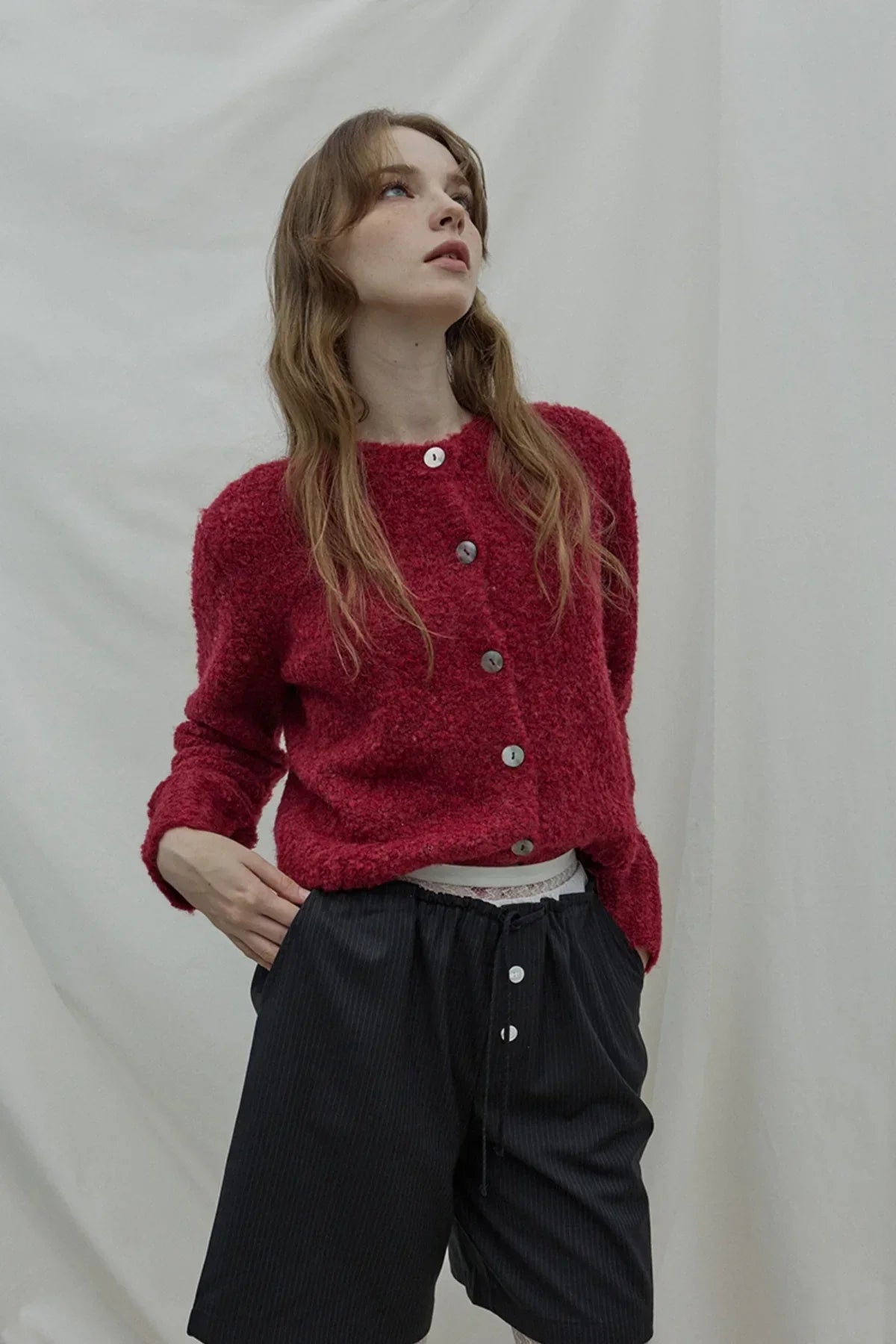 Woman wearing a textured wine-colored cardigan with black buttoned shorts against a plain backdrop