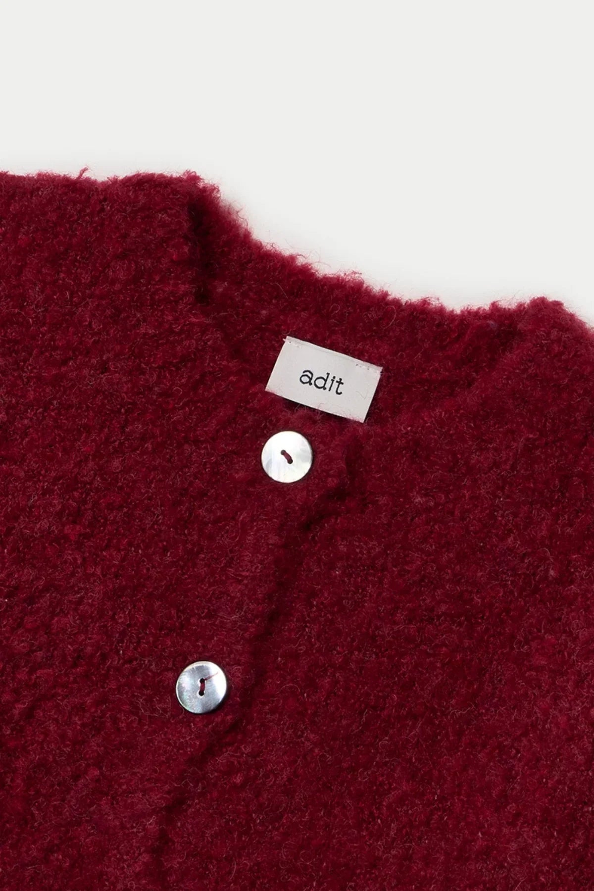 Close-up of wine red textured grandma cardigan with two white buttons and adit brand label