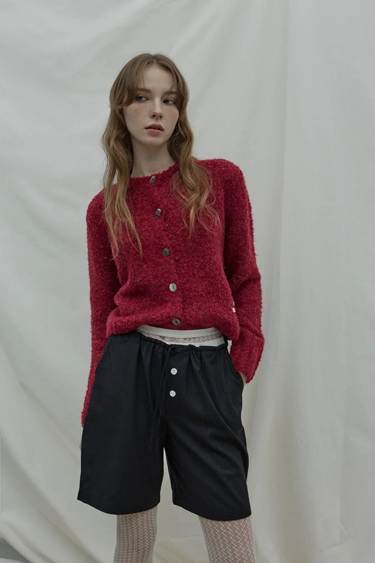 Fashion model wearing wine red textured grandma cardigan with black shorts and white textured tights