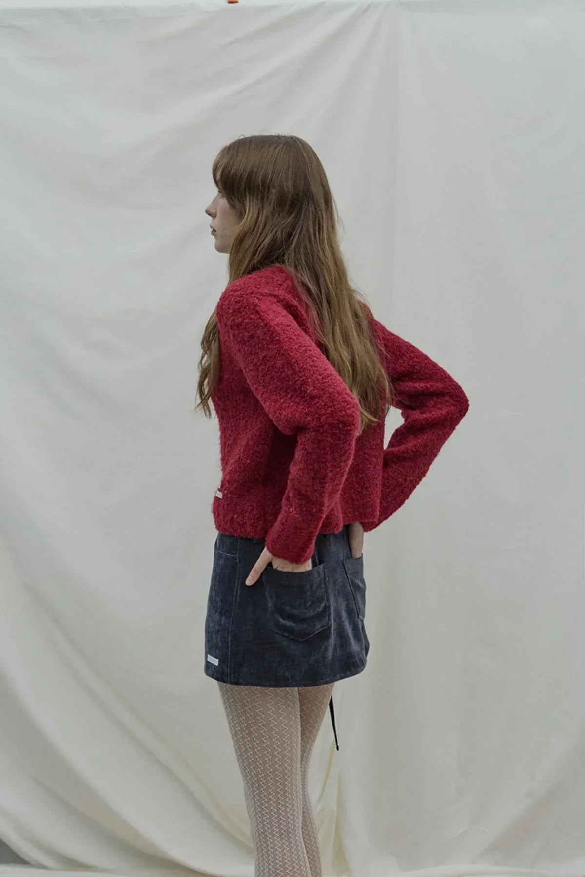 Woman wearing a wine-colored fuzzy grandma cardigan, navy mini skirt, and patterned tights
