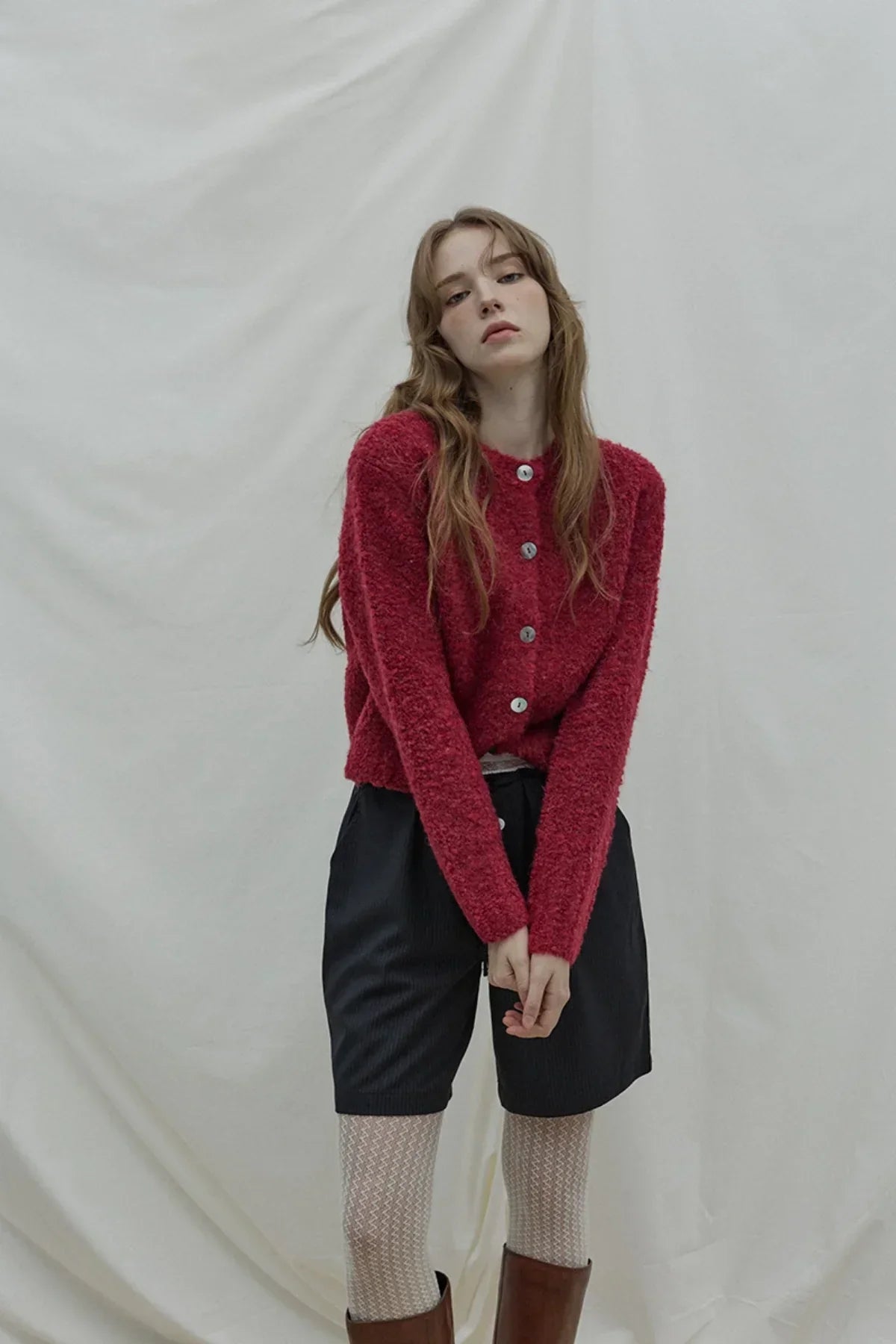 Young woman wearing a wine-colored fuzzy button-up cardigan with black shorts and patterned tights