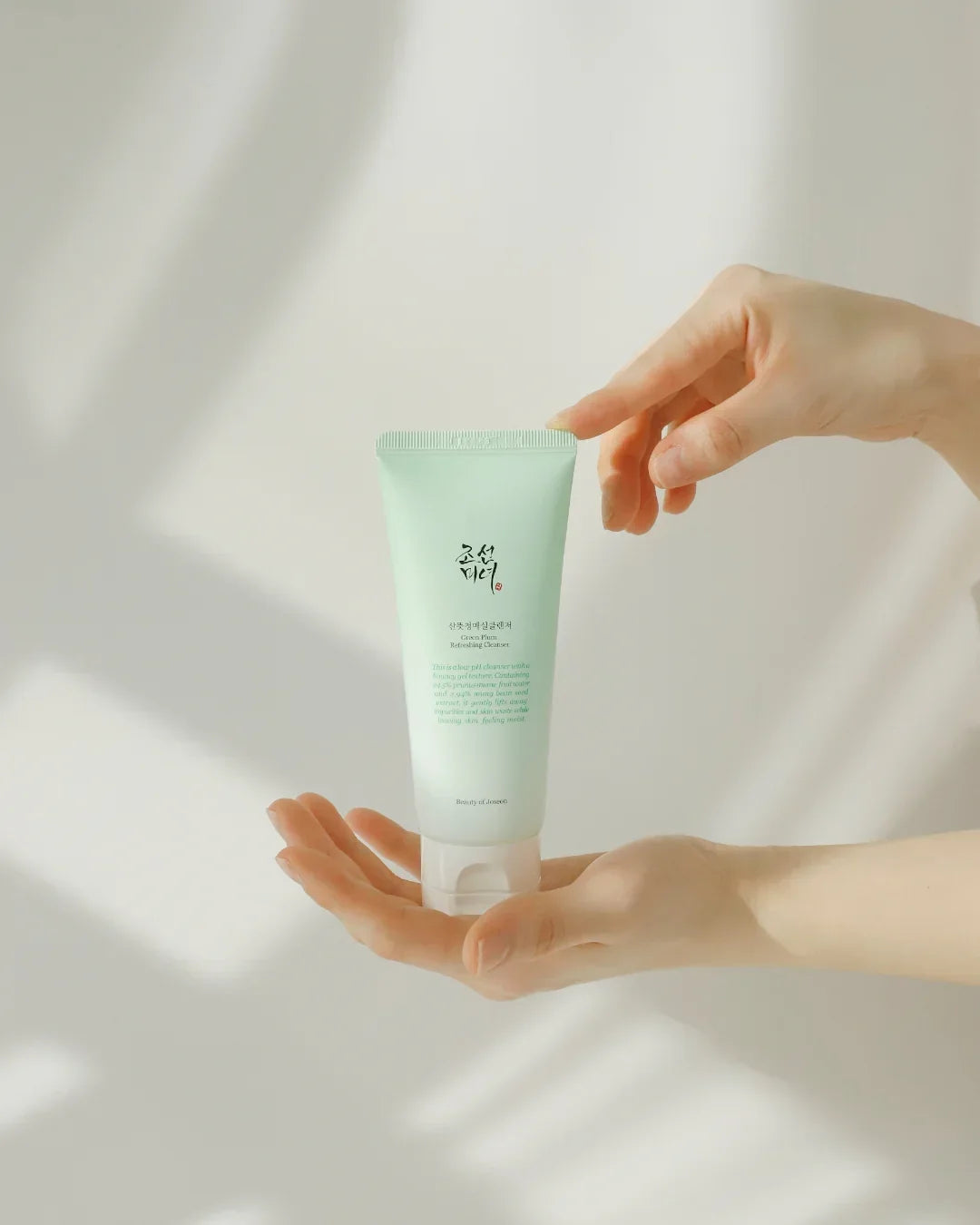 Person holding light green tube of Green Plum Refreshing Cleanser with soft natural light