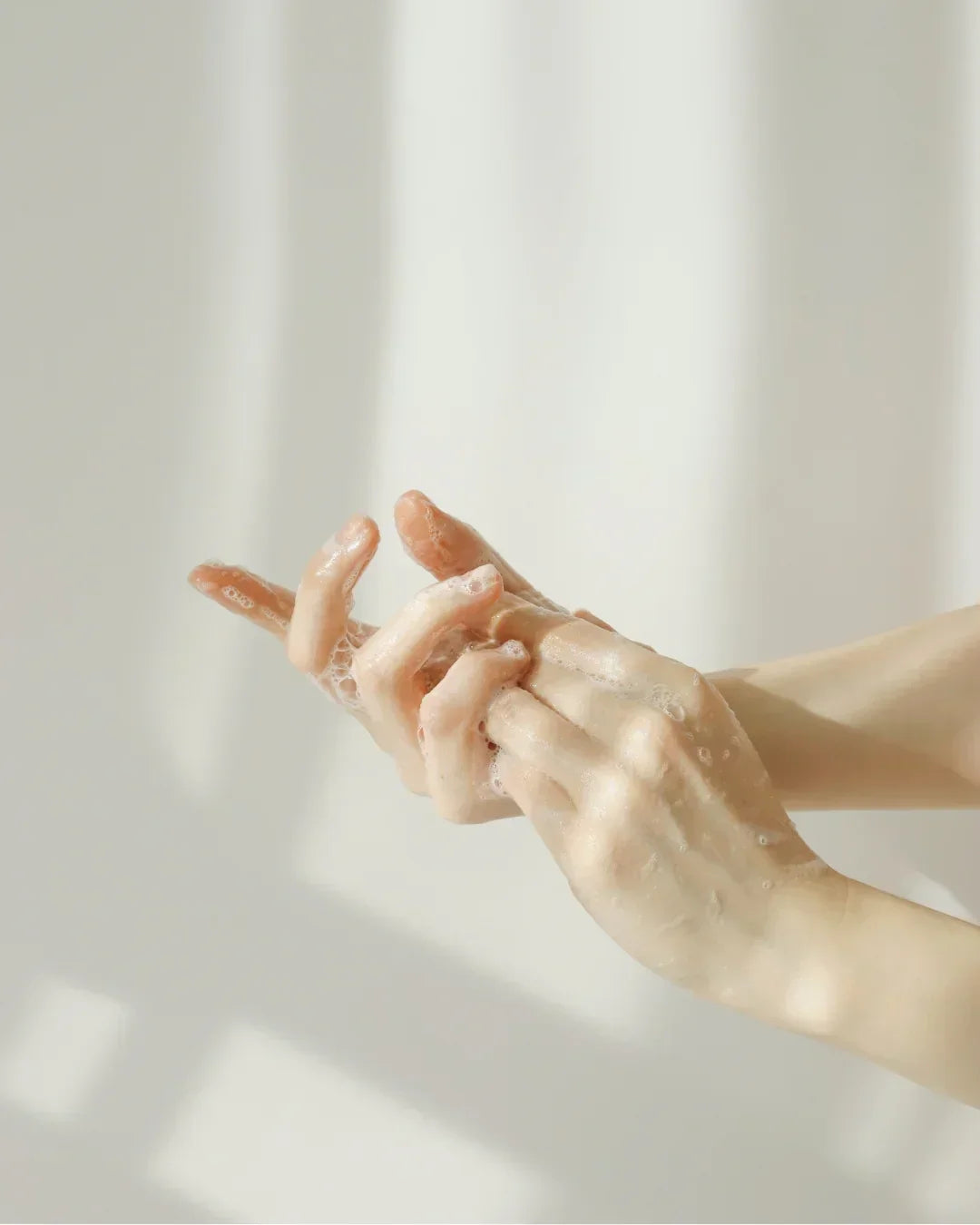 Close-up of hands covered in foamy soap bubbles against soft natural light background