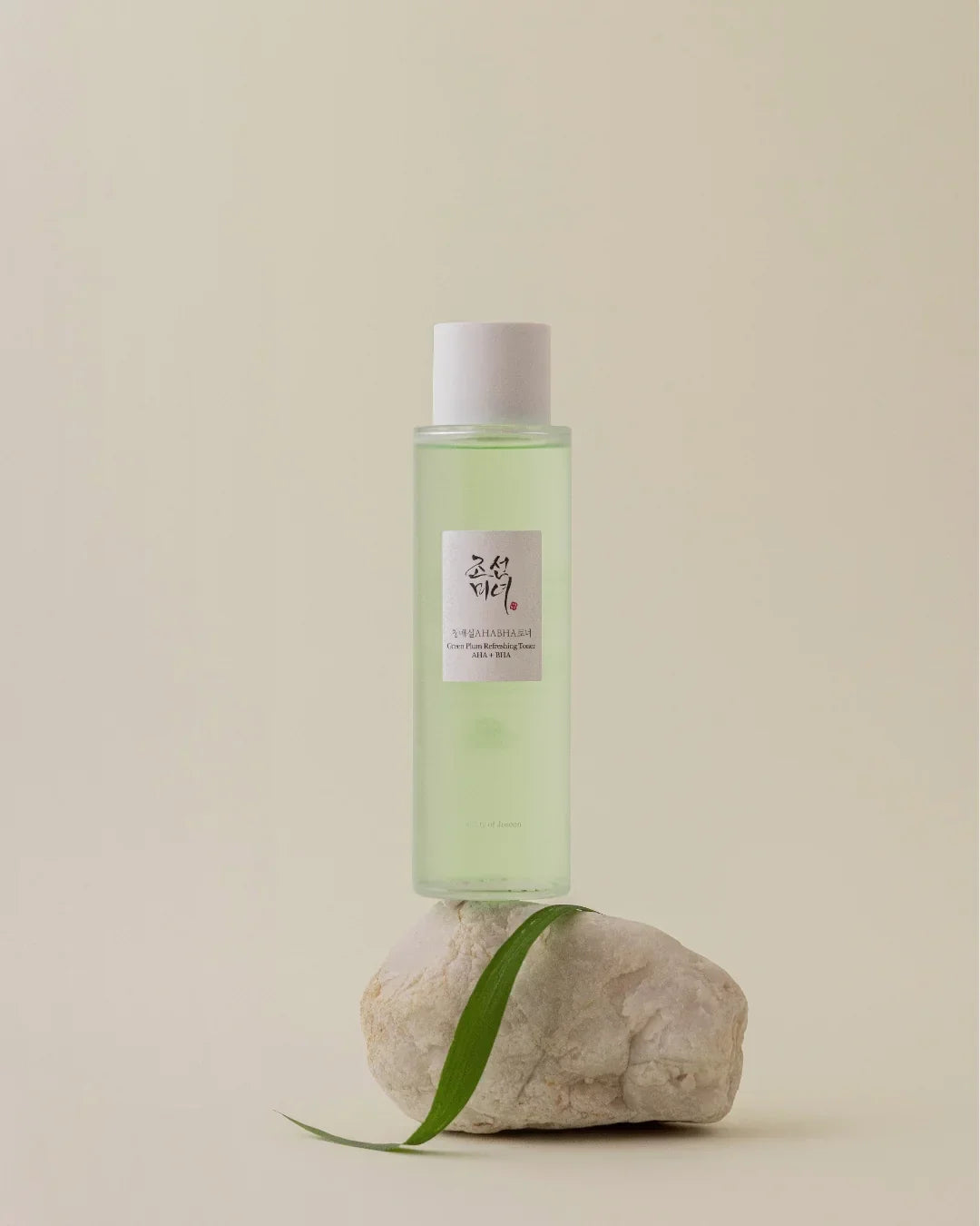 Green Plum Refreshing Toner AHA BHA bottle on white stone with green leaf, minimalist background