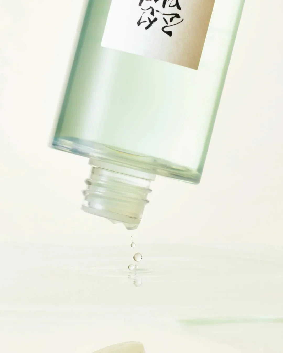 Green tinted toner bottle pouring clear liquid droplets on reflective surface