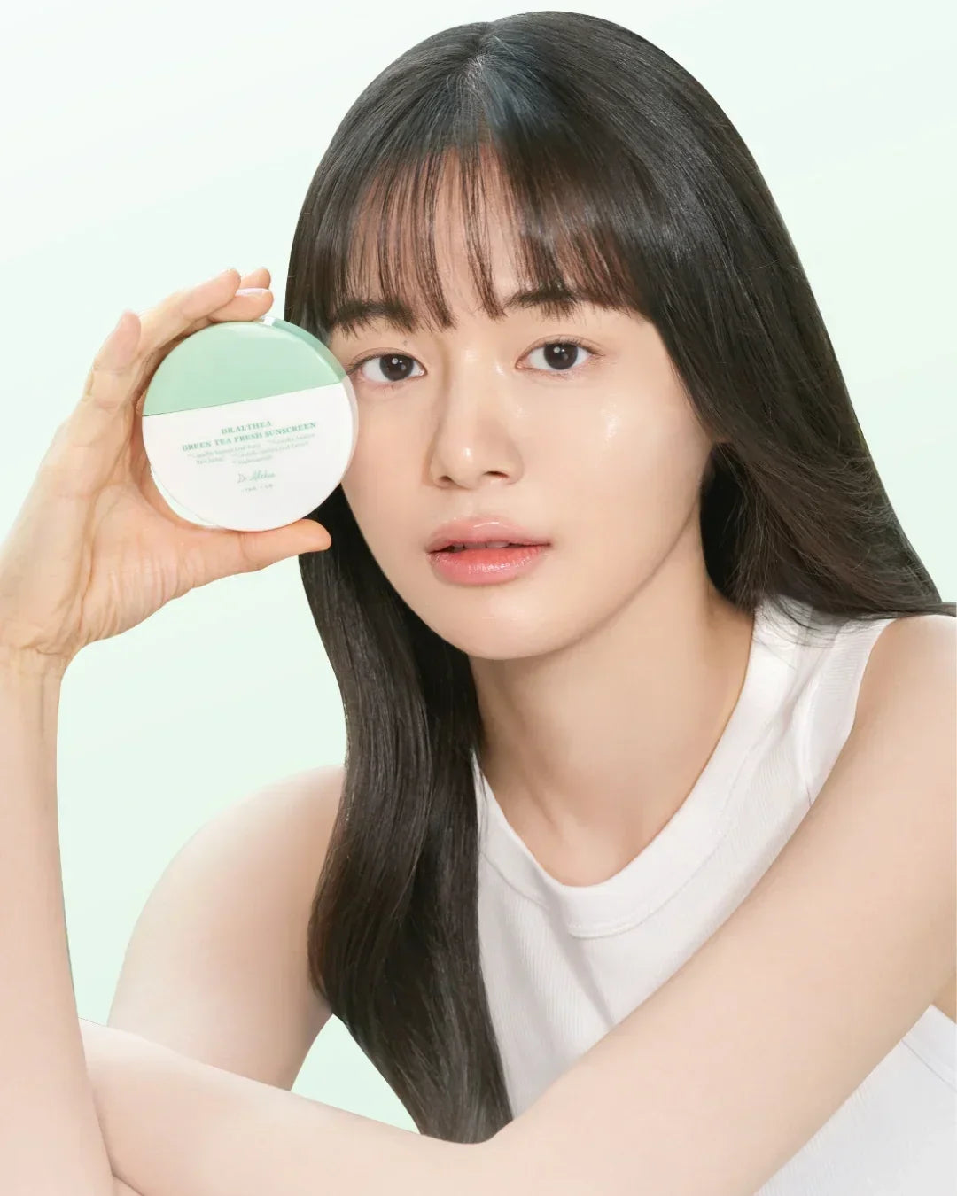 Young woman with long dark hair holding Brazalya green tea fresh sunscreen compact, natural skincare