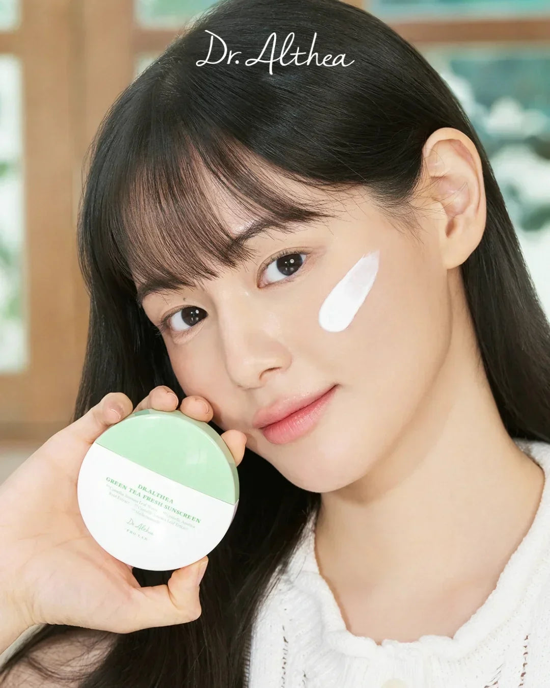 Woman with clear skin holding Dr. Althea Green Tea Fresh Sunscreen with cream on cheek