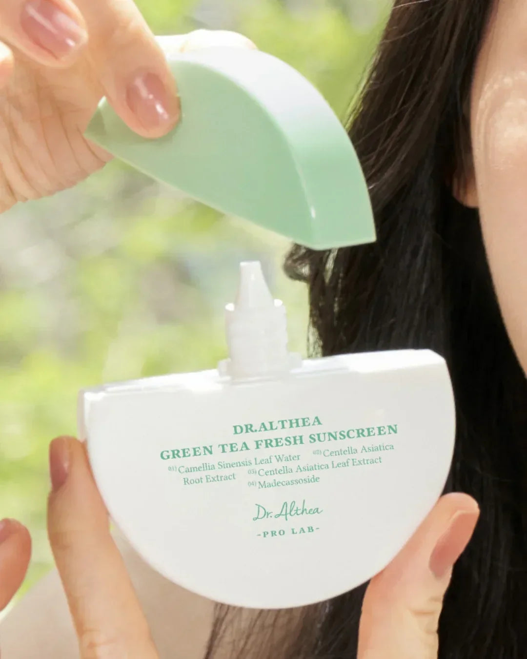 Hand holding Dr Althea Green Tea Fresh Sunscreen with green cap against blurred natural background