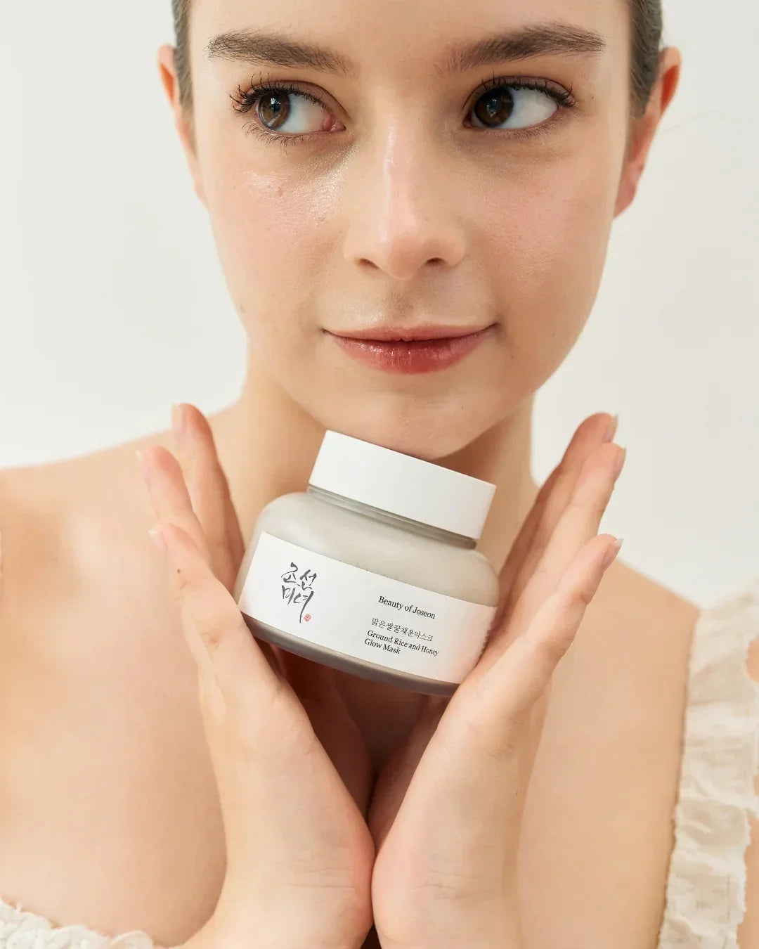 Young woman holding Beauty of Joseon Ground Rice and Honey Glow Mask jar near her face