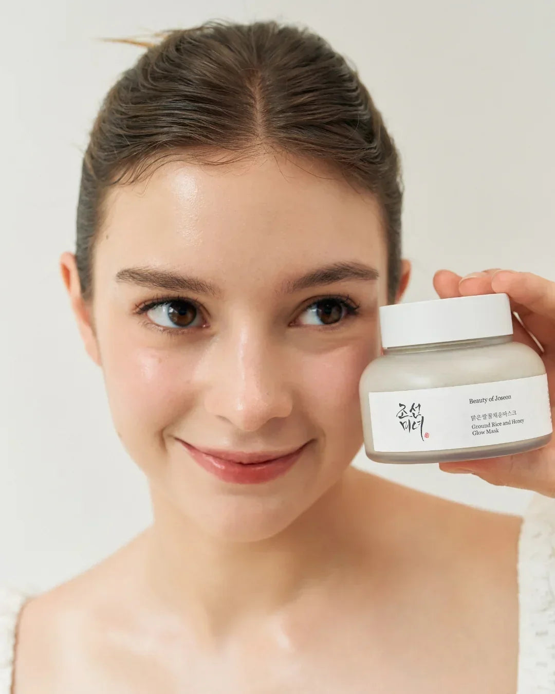 Smiling woman with clear skin holding Beauty of Joseon Ground Rice and Honey Glow Mask jar