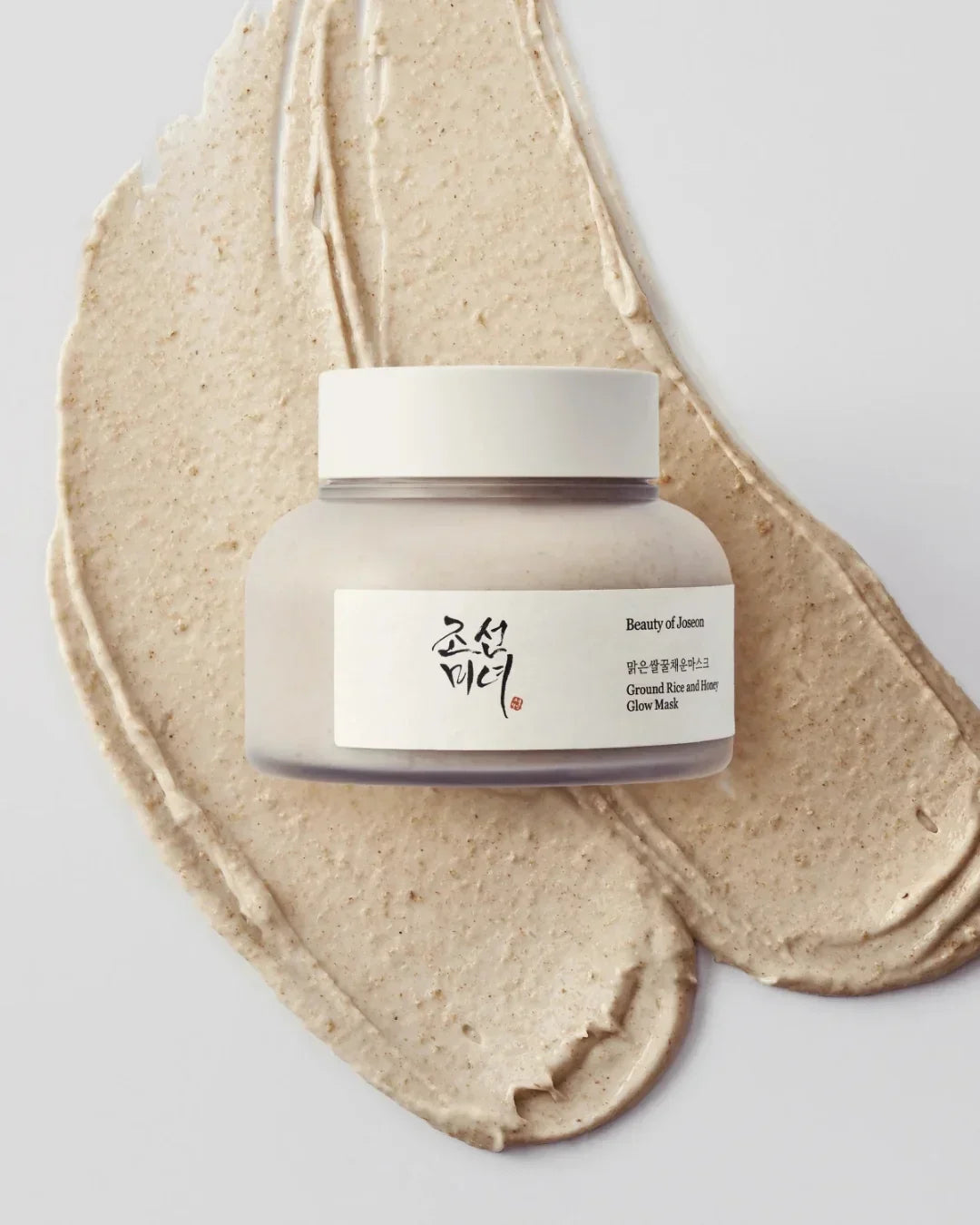 Beauty of Joseon Ground Rice and Honey Glow Mask jar on textured cream mask spread on white surface