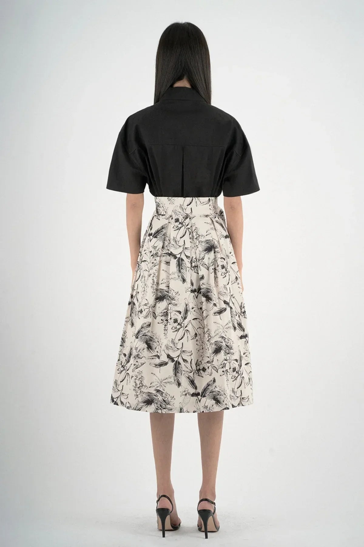 Back view of woman wearing black short-sleeved shirt and high-waisted floral print skirt with heels