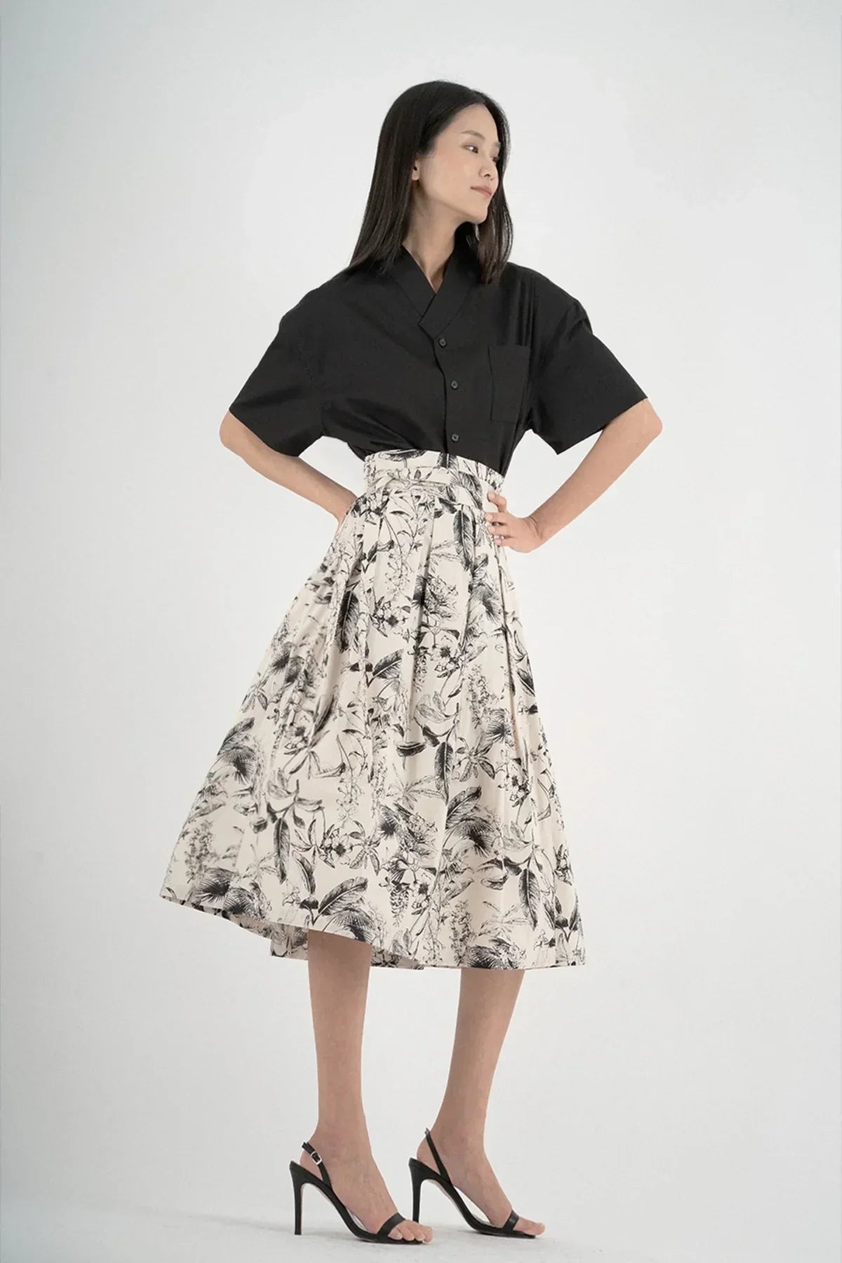 Woman wearing black short-sleeved shirt with collar and floral print midi skirt in studio