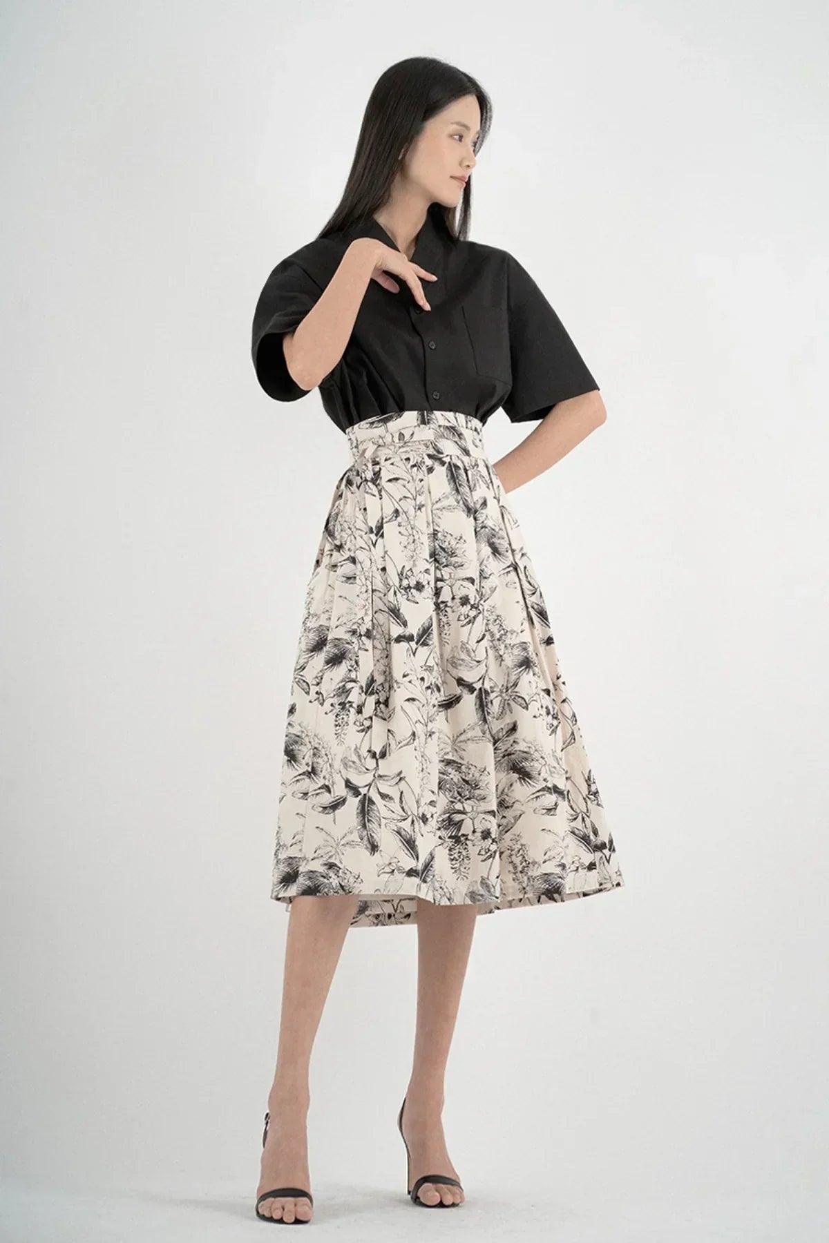 Woman wearing black short-sleeved shirt and floral high-waisted midi skirt in studio