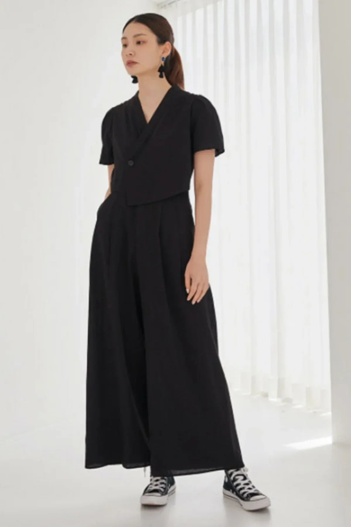 Woman wearing a black wide-leg jumpsuit with short sleeves and sneakers in a bright room