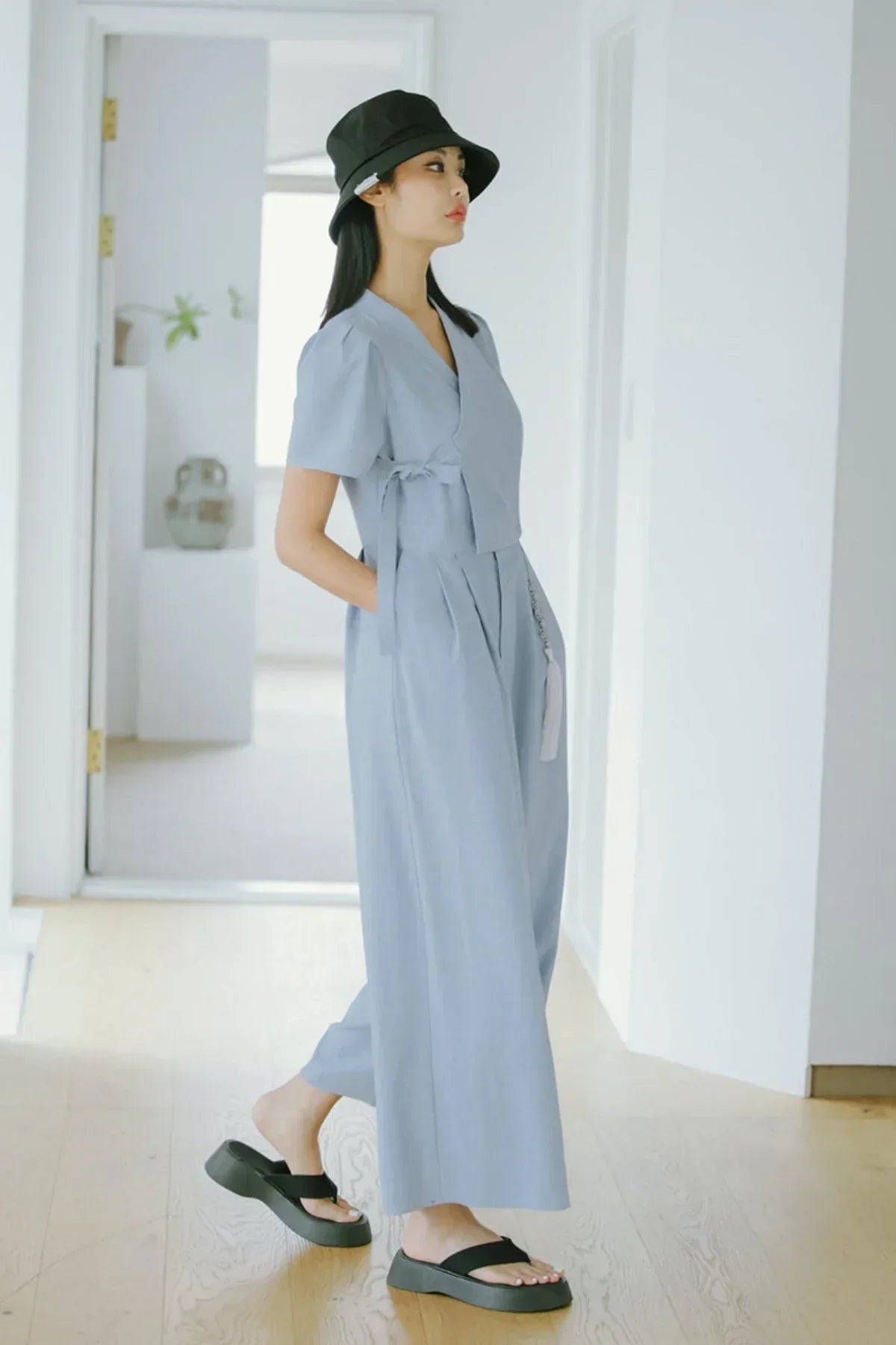 Woman wearing light blue jumpsuit with short sleeves, black bucket hat, and black platform sandals indoors