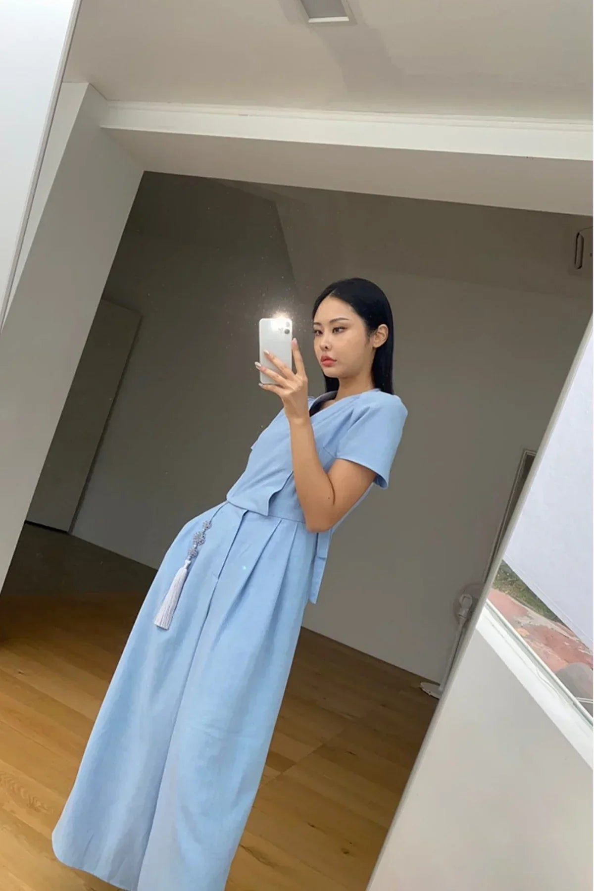 Woman taking mirror selfie wearing a light blue Hanaui jumpsuit in minimalist room with wooden floor