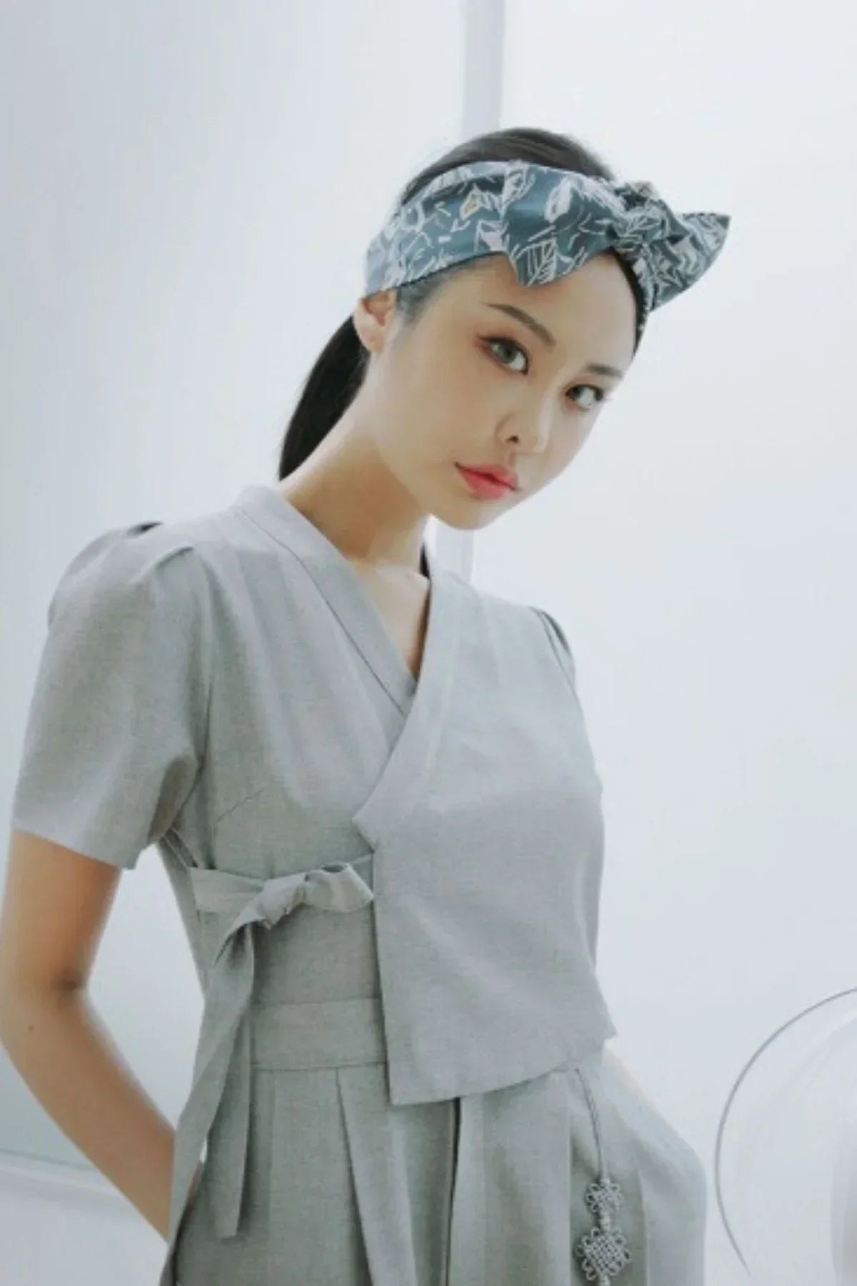 Woman wearing gray wrap top and pants with patterned headband in minimalistic setting