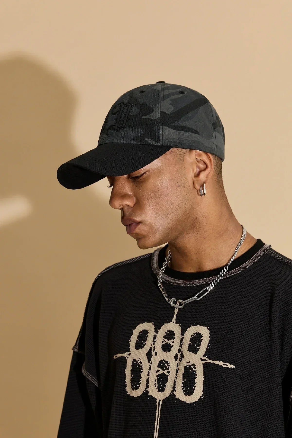 Young man wearing a black and grey camo baseball cap, black graphic shirt, and silver chain necklace