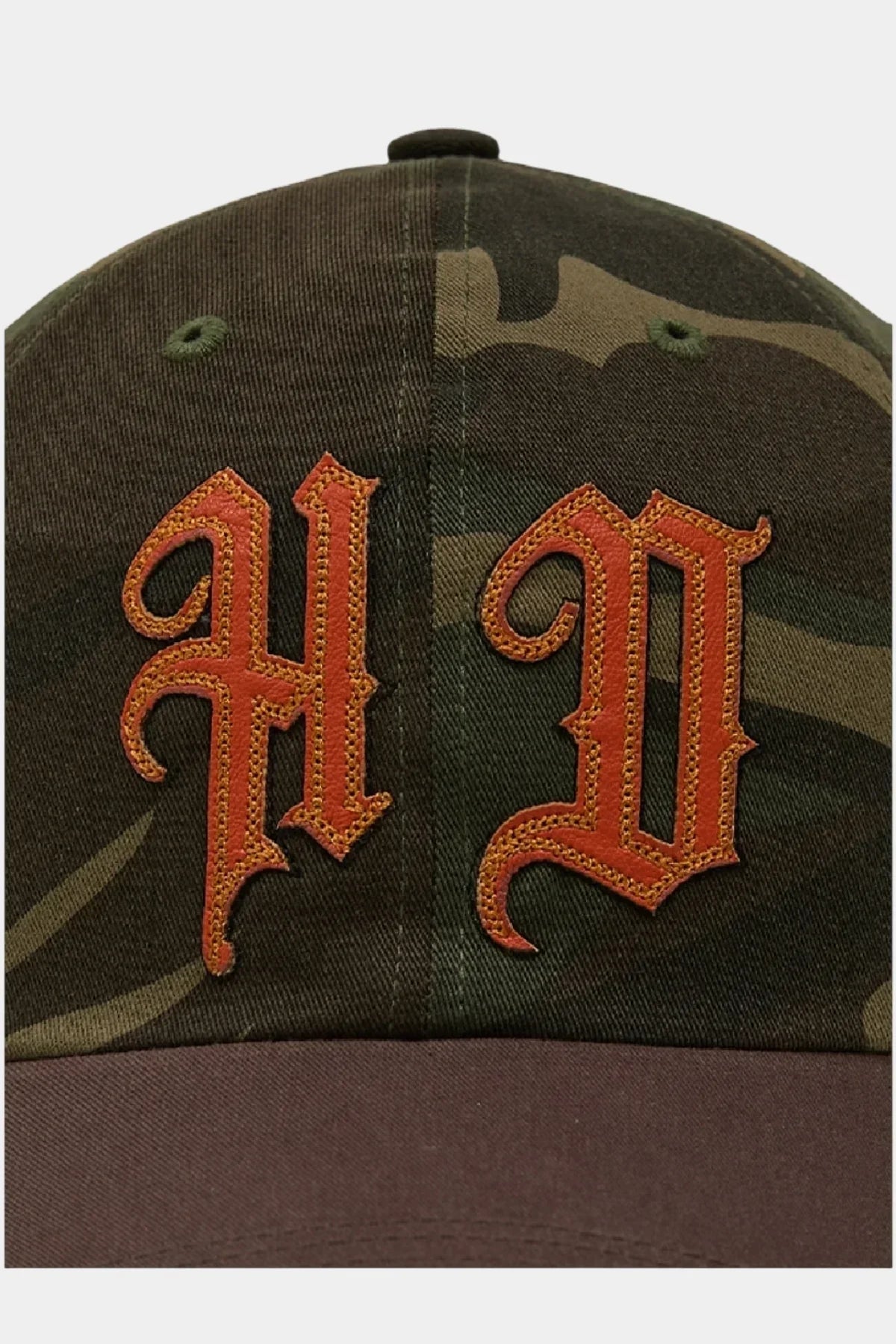 Close-up of camo ball cap with brown brim featuring orange stitched 'A' and 'D' appliques