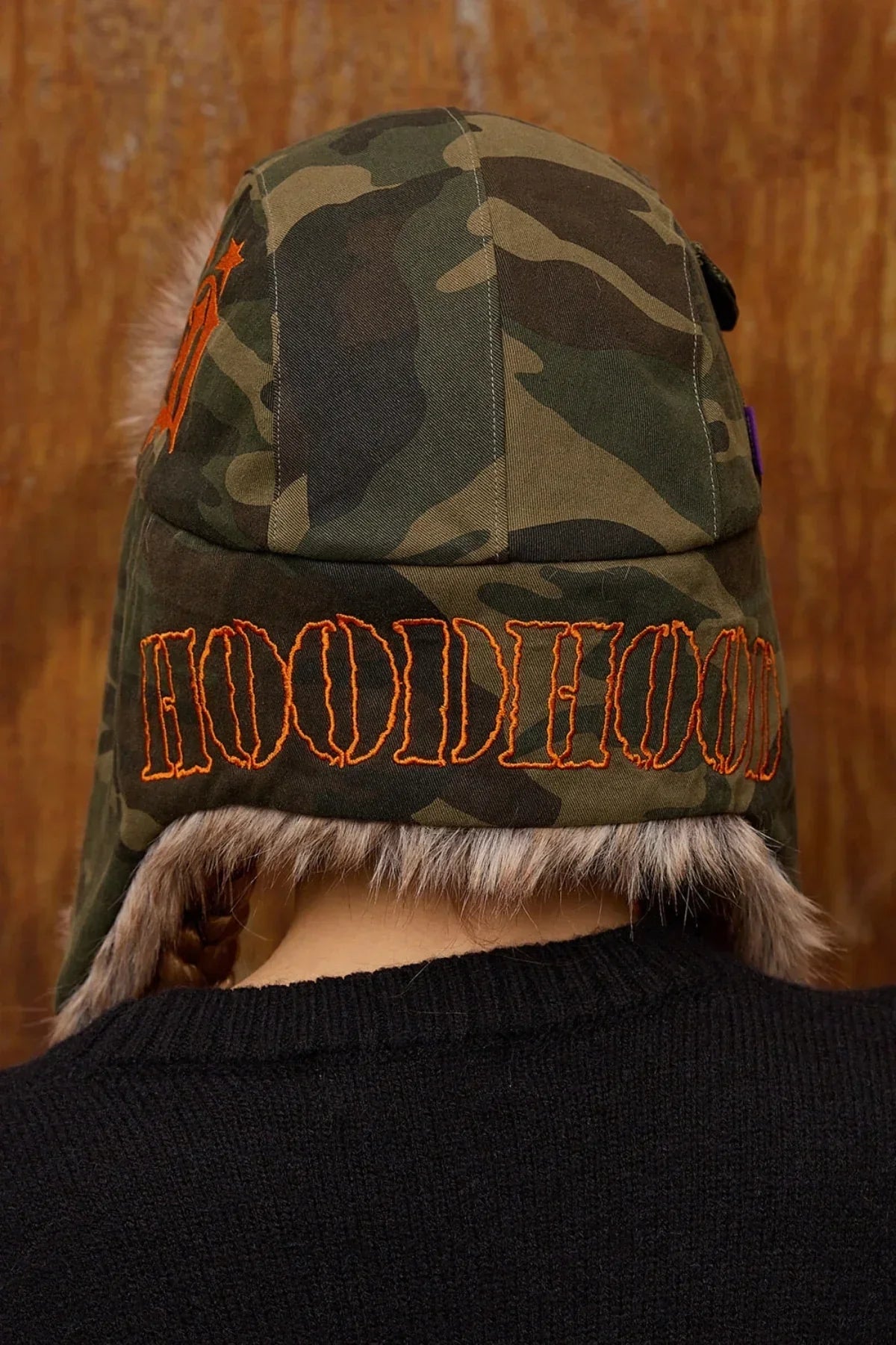 Back view of camo fur trooper hat with orange embroidered HOODIEHOOD logo and faux fur trim