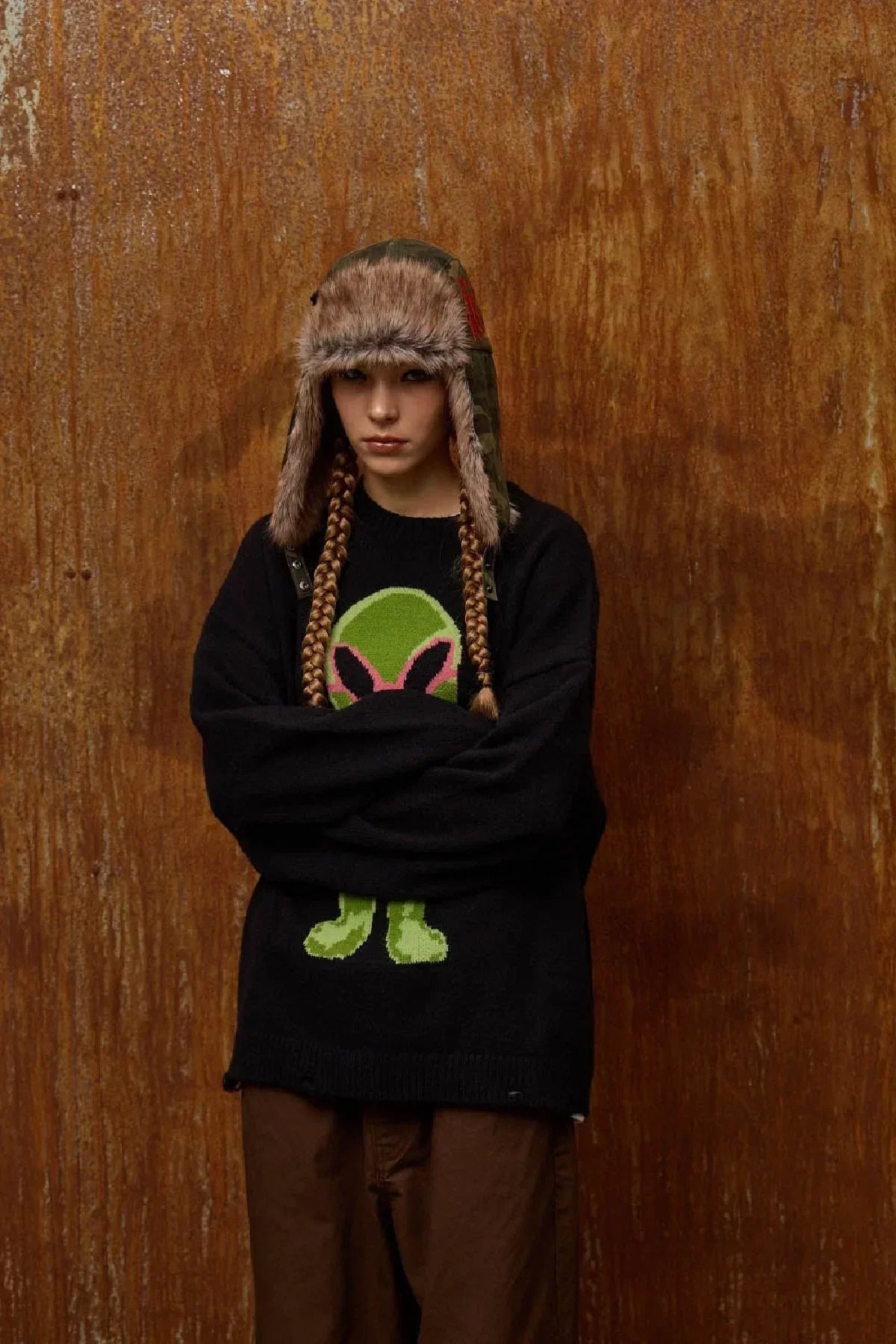 Model wearing camo winter fur trooper hat and black sweater with green bunny graphic, brown pants