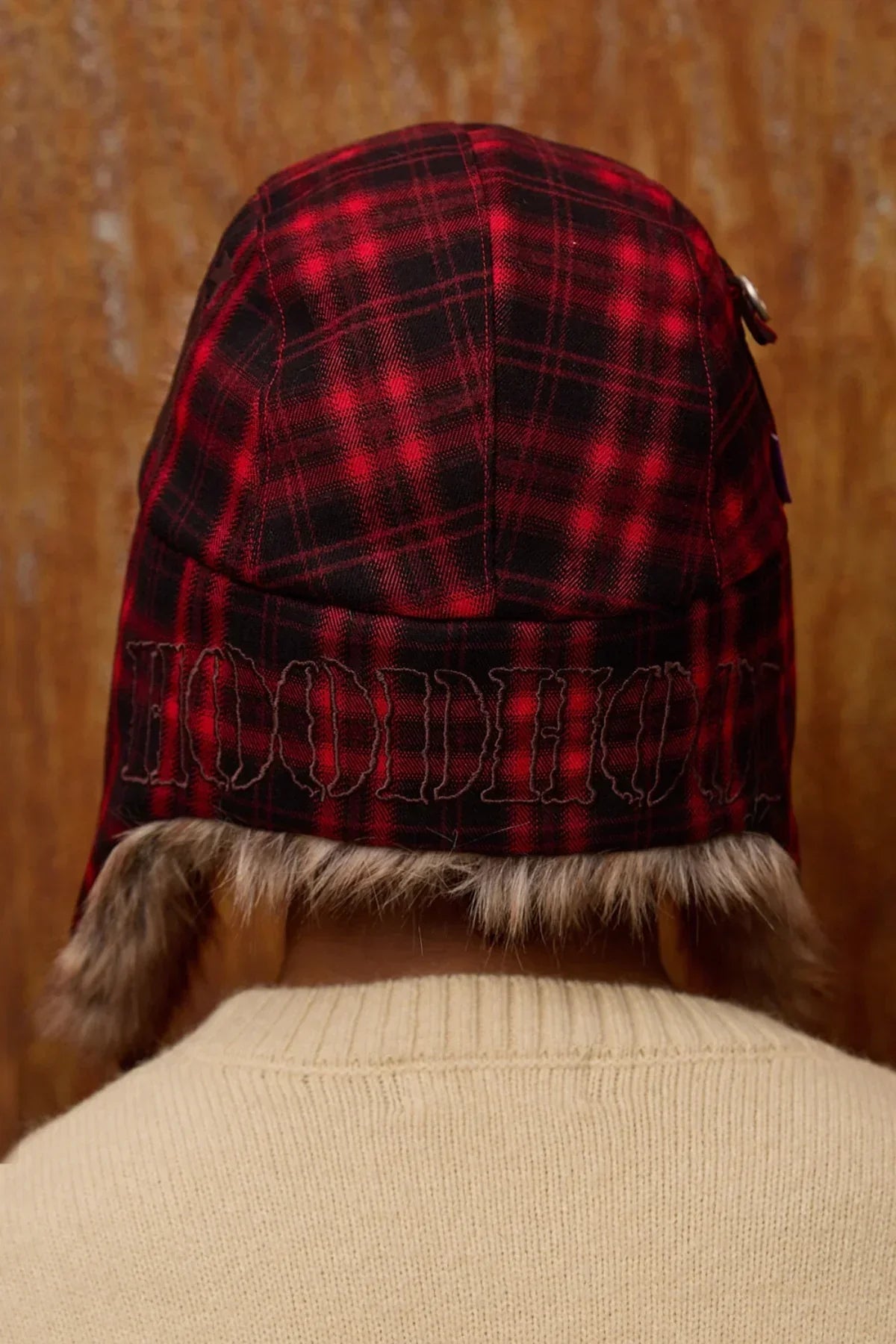 Back view of person wearing red and black plaid fur trooper hat with beige sweater