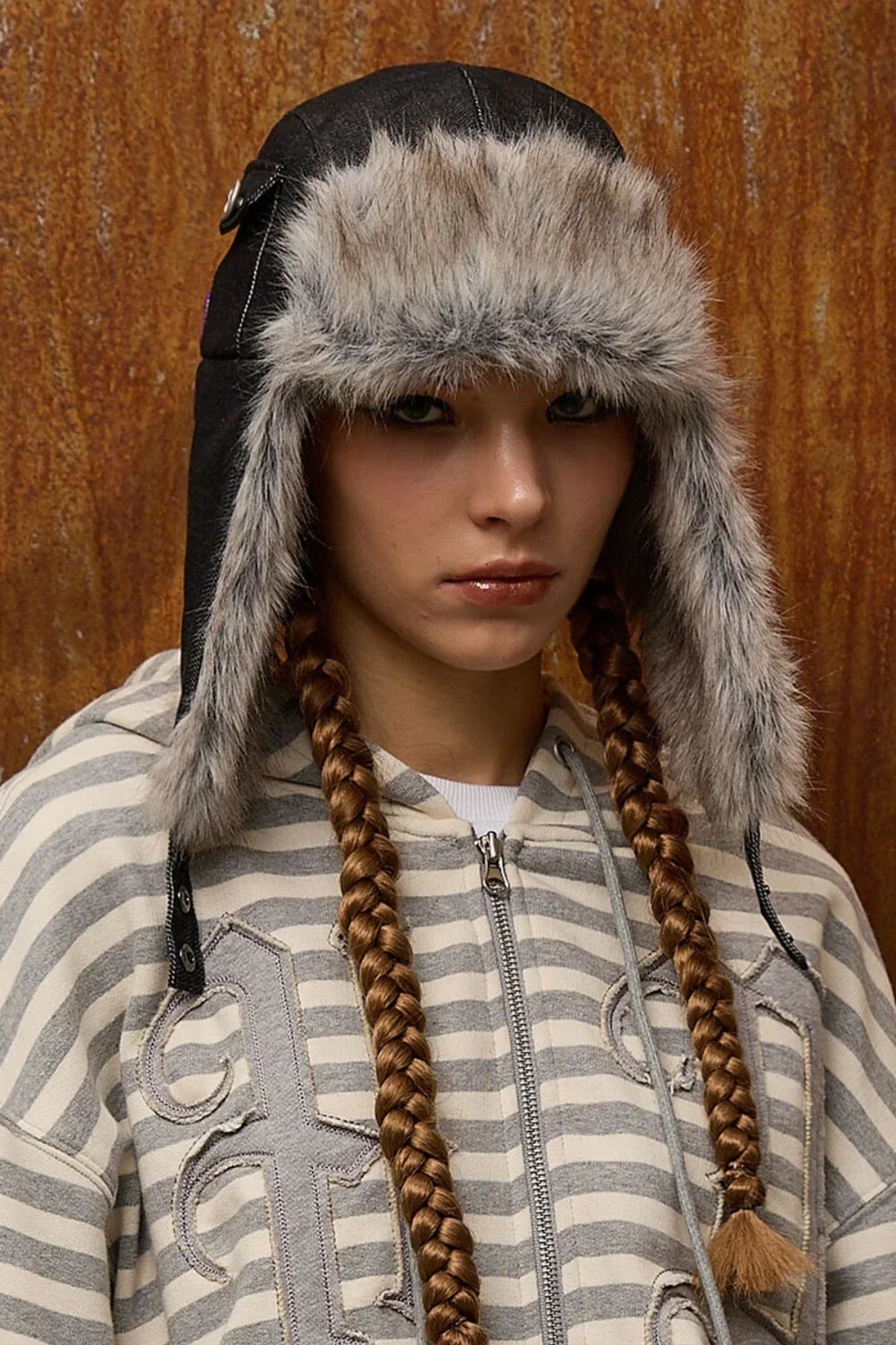 Woman with long braids wearing a black fur-trimmed trooper hat and striped zip-up hoodie
