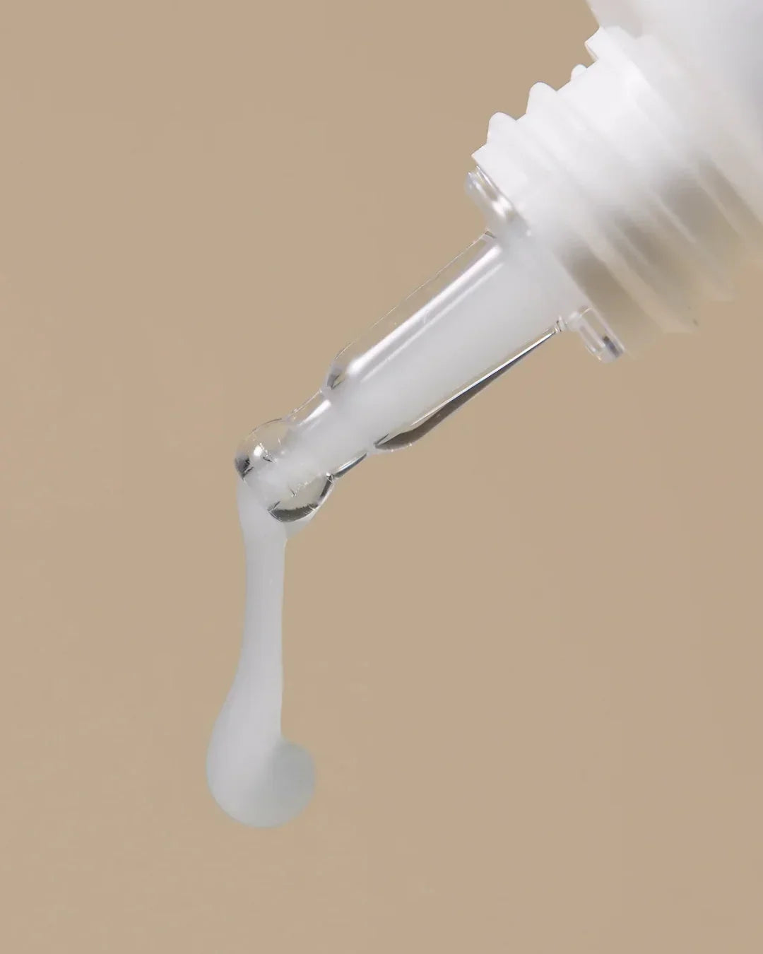Close-up of white cream dropping from a clear applicator tip against a beige background