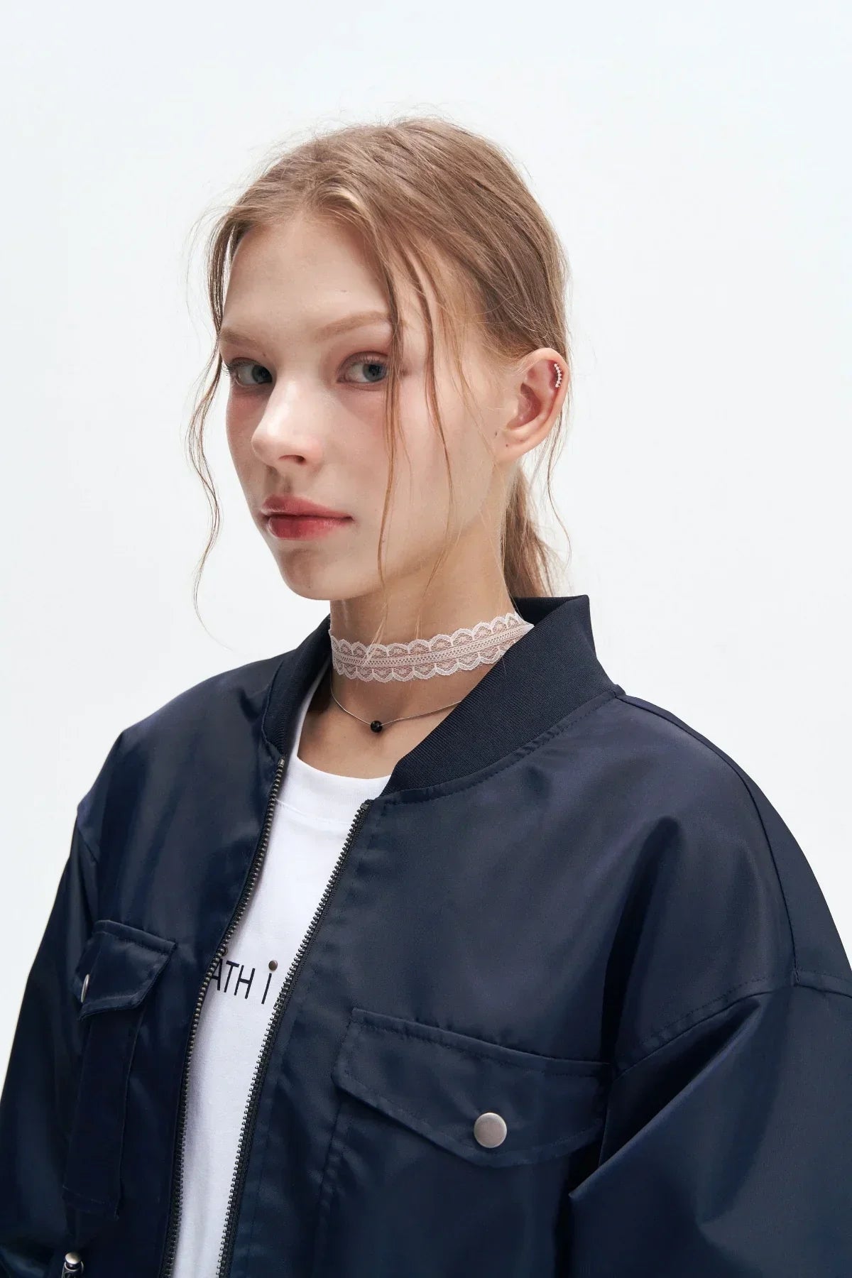 Close-up of a young woman wearing a navy heavy nylon bomber jacket with flap pockets and white shirt