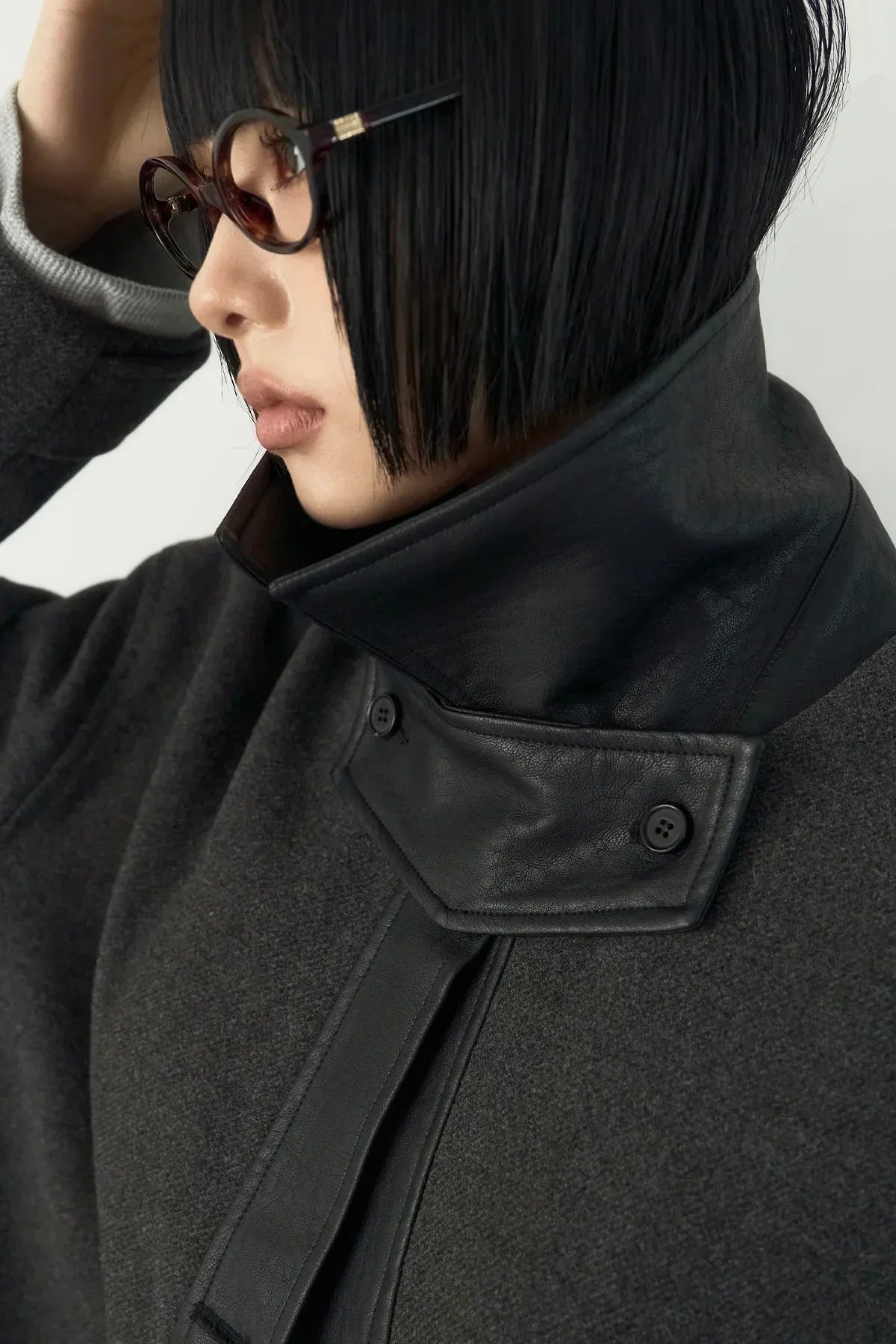 Close-up of person wearing high-neck dark gray coat with black leather collar and eyeglasses