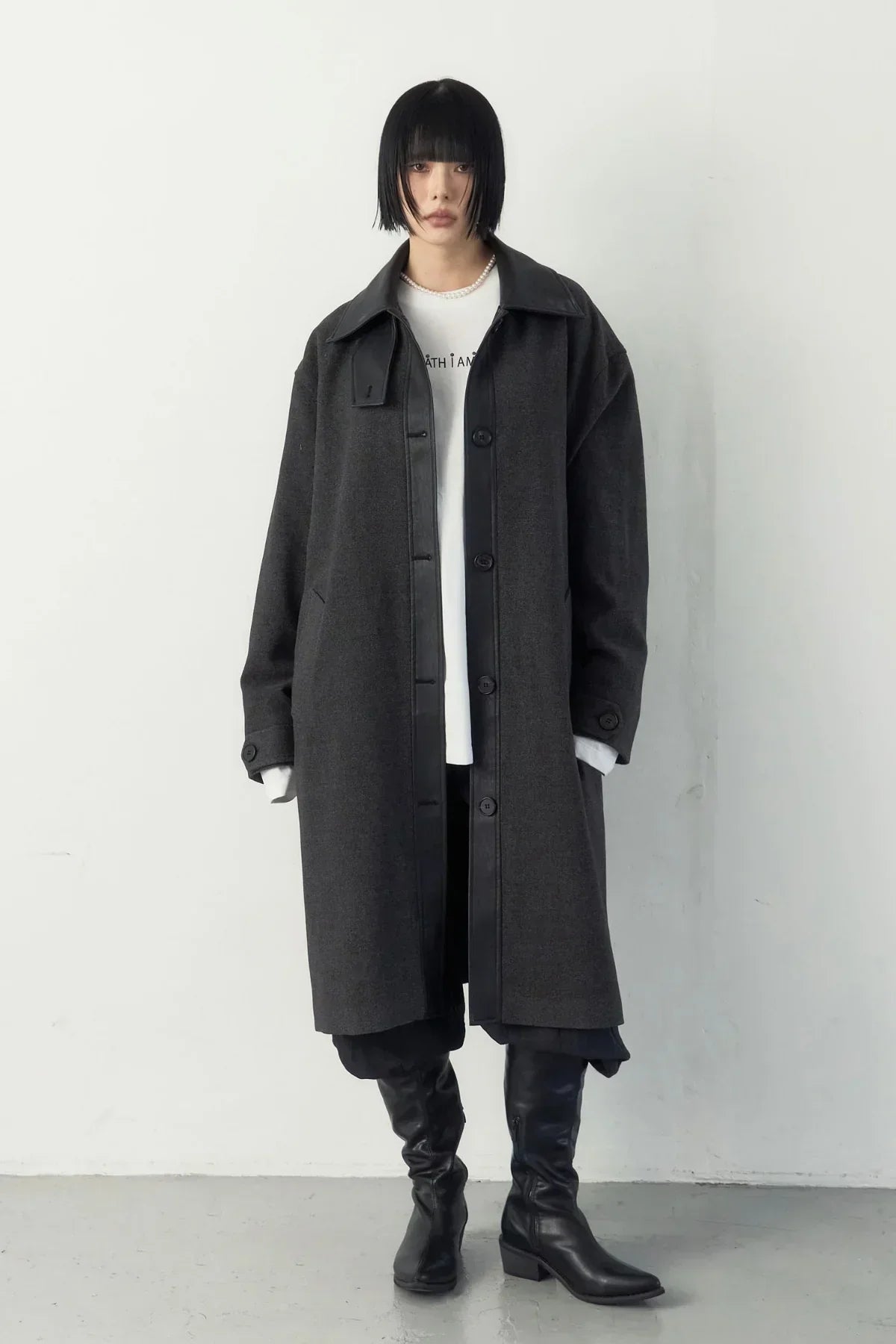 Model wearing dark gray long coat with black leather trim, white shirt, black pants, and knee-high black boots