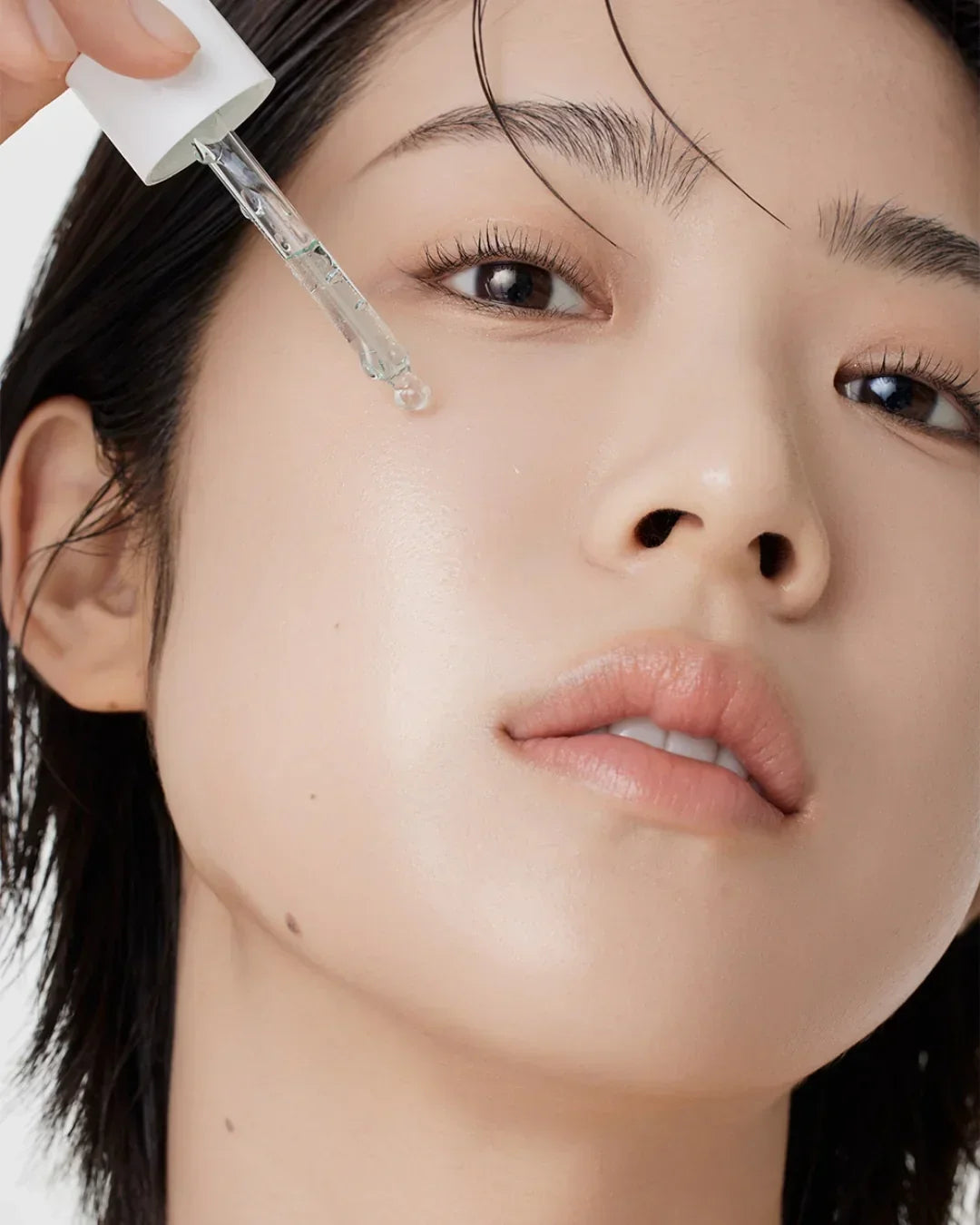 Close-up of woman applying clear hyssop serum with dropper on smooth skin