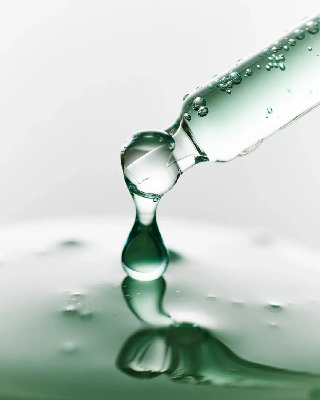 Close-up of clear serum drop falling from glass dropper with bubbles in liquid