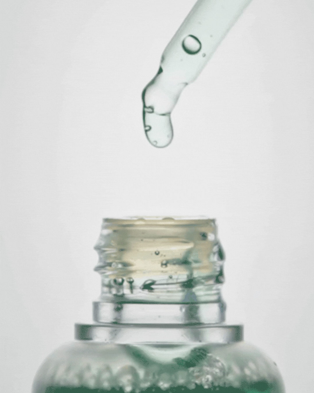 Close-up of clear serum dropper releasing liquid drop into open cosmetic bottle