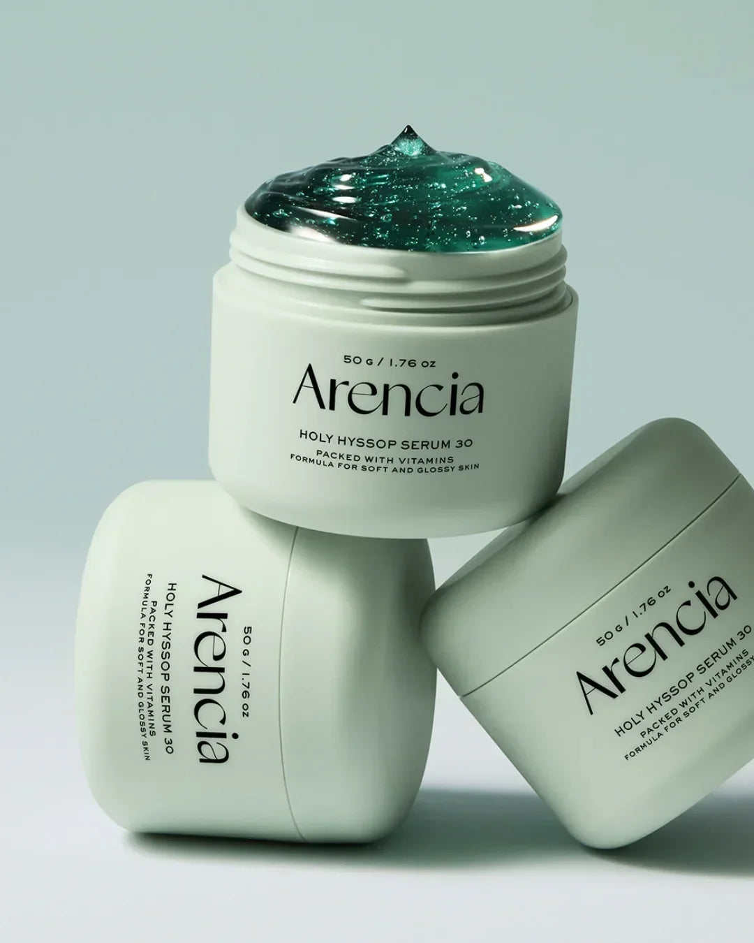 Three white jars of Arencia Holy Hyssop Serum 30 with green gel serum on top jar on light background