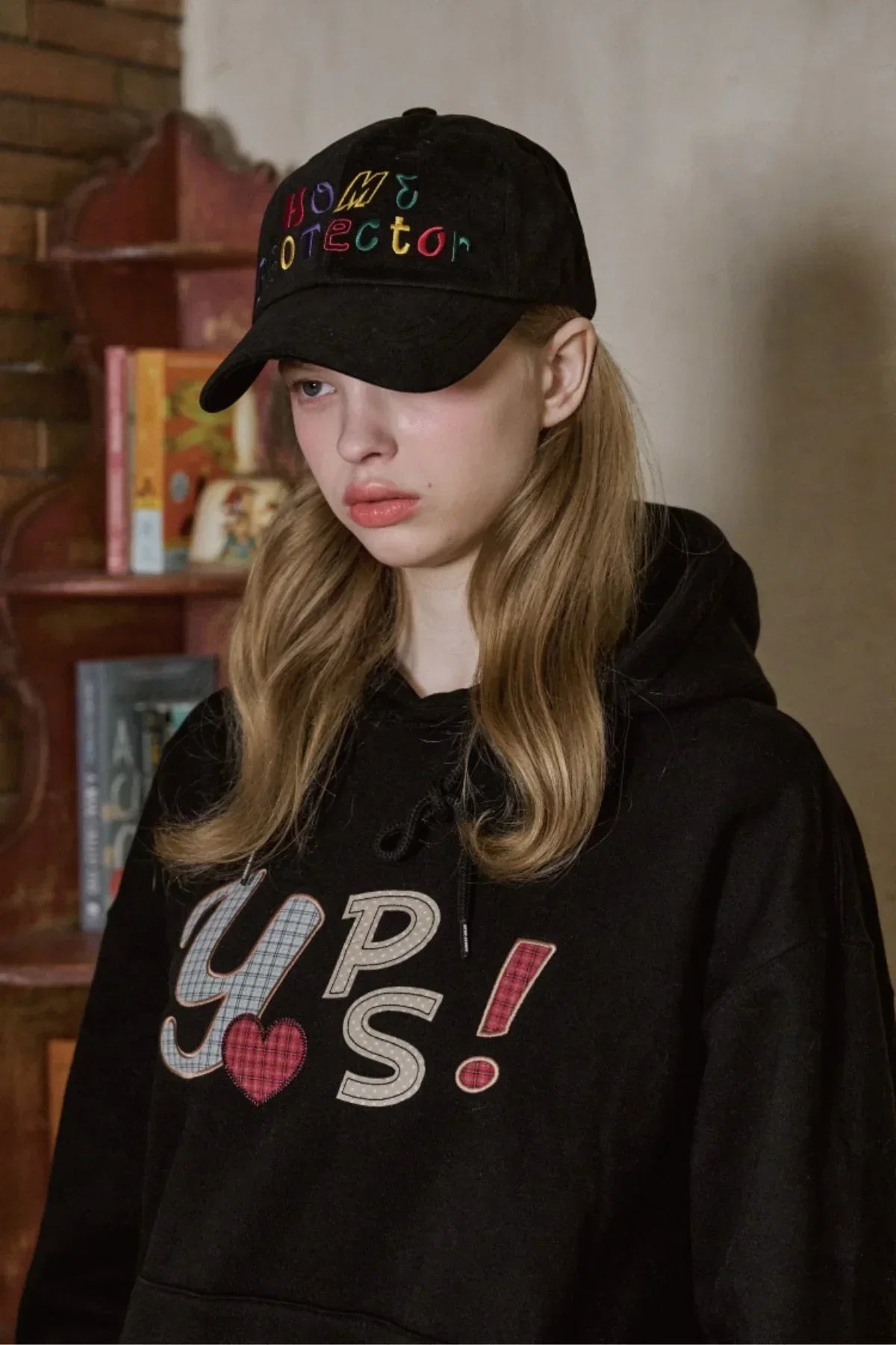 Young woman wearing black ballcap with colorful Home Protector embroidery and black hoodie with Y P S text