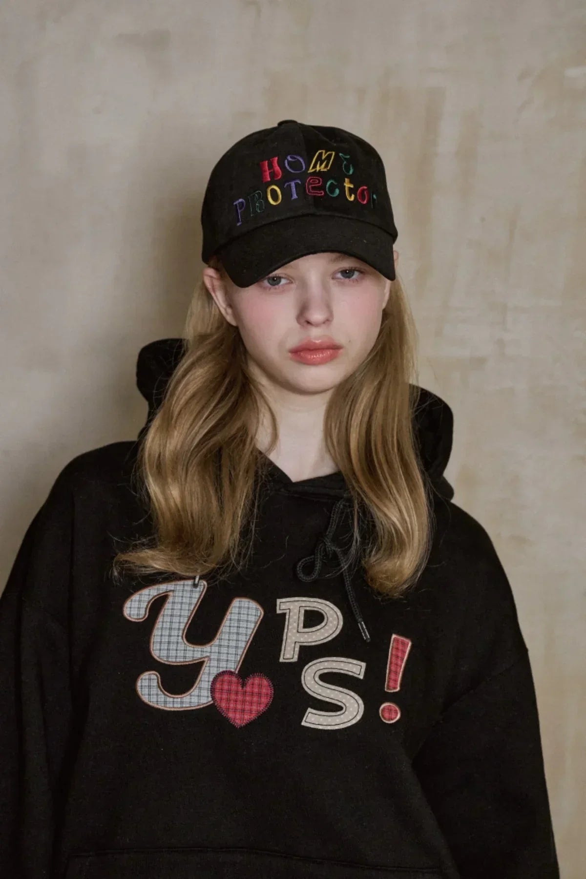 Young woman wearing black baseball cap with colorful Home Protector logo and black hoodie with YPS text