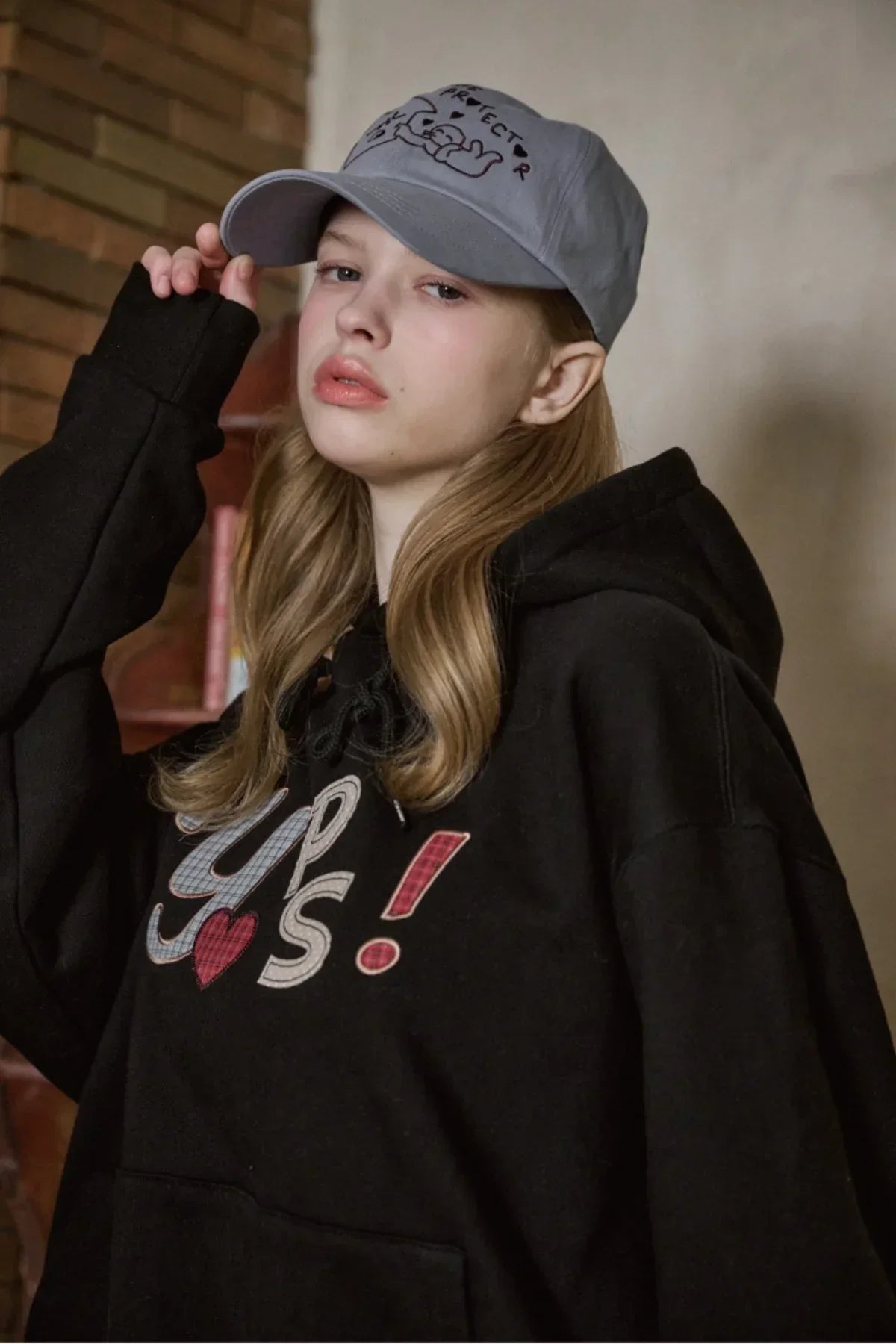 Young woman wearing sky blue baseball cap with cat design and black hoodie with colorful text