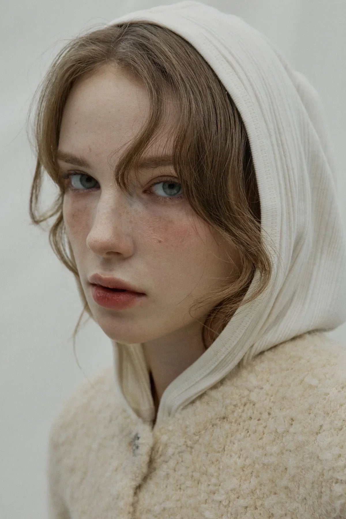 Close-up of woman wearing natural cream ribbed hooded cardigan and textured wool coat