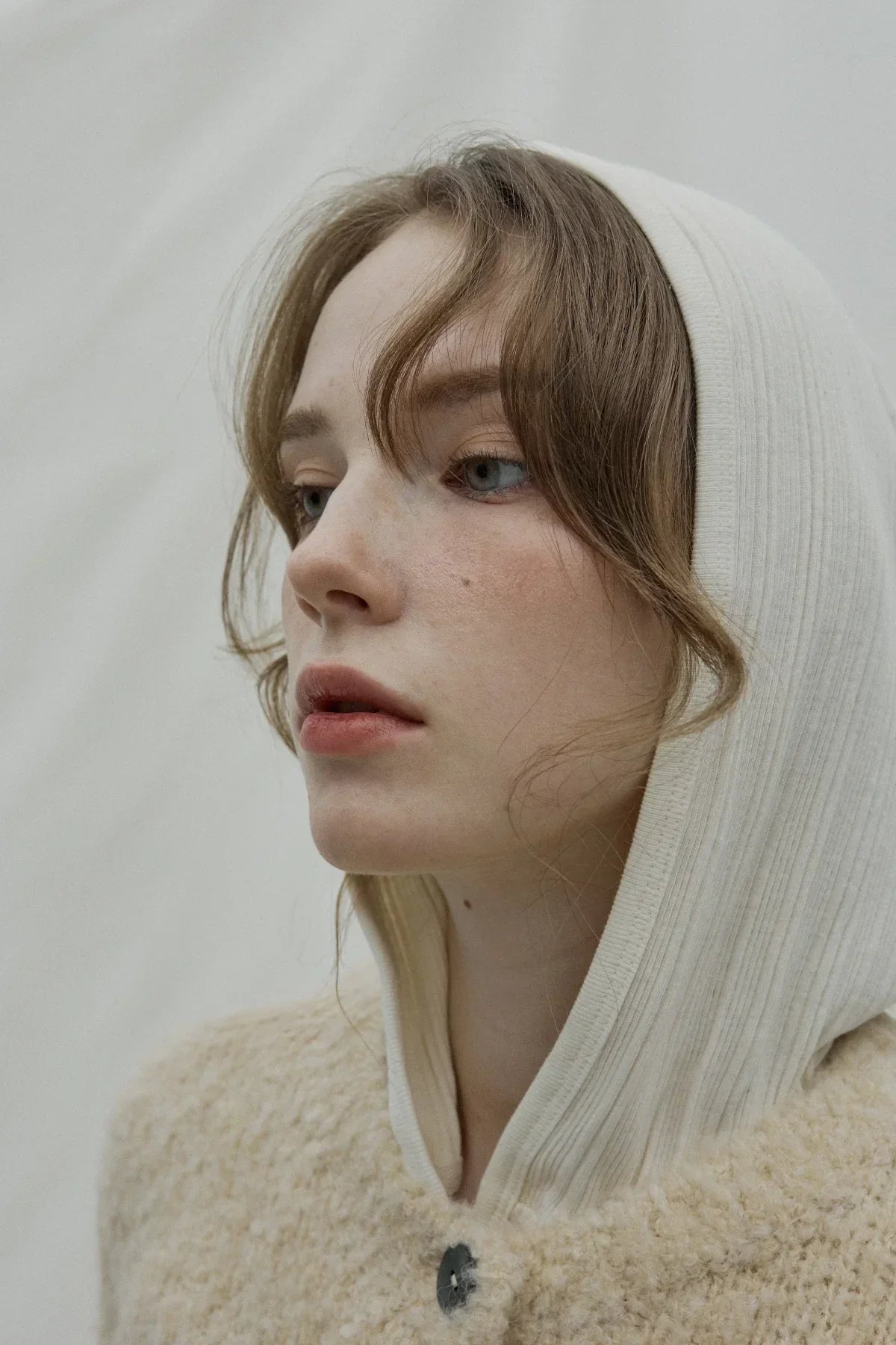 Close-up of woman wearing a natural cream ribbed hooded cardigan with a buttoned front