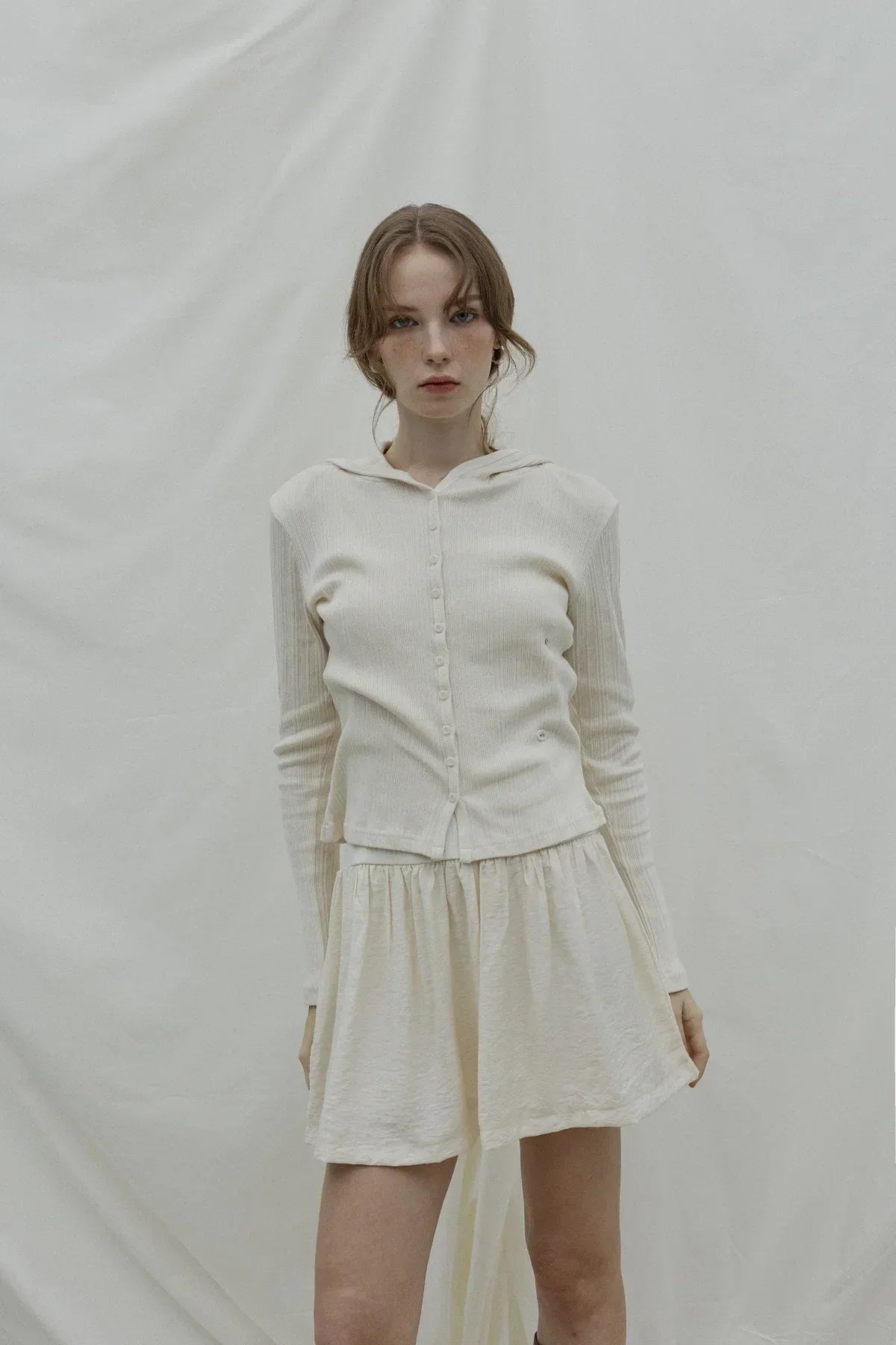 Model wearing natural cream ribbed hooded cardigan and matching skirt against beige backdrop