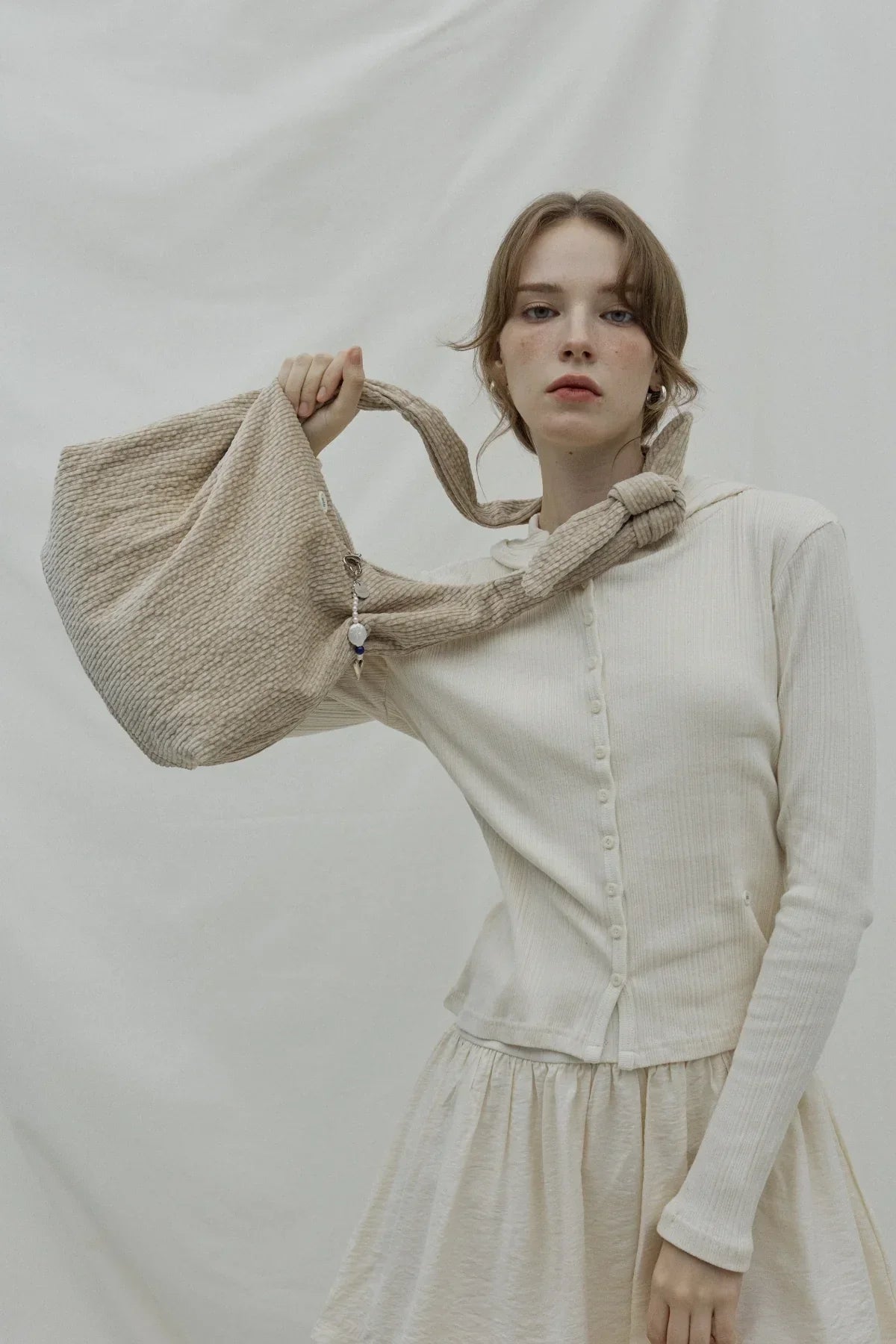 Woman wearing cream ribbed cardigan and skirt holding beige textured handbag with bead charm